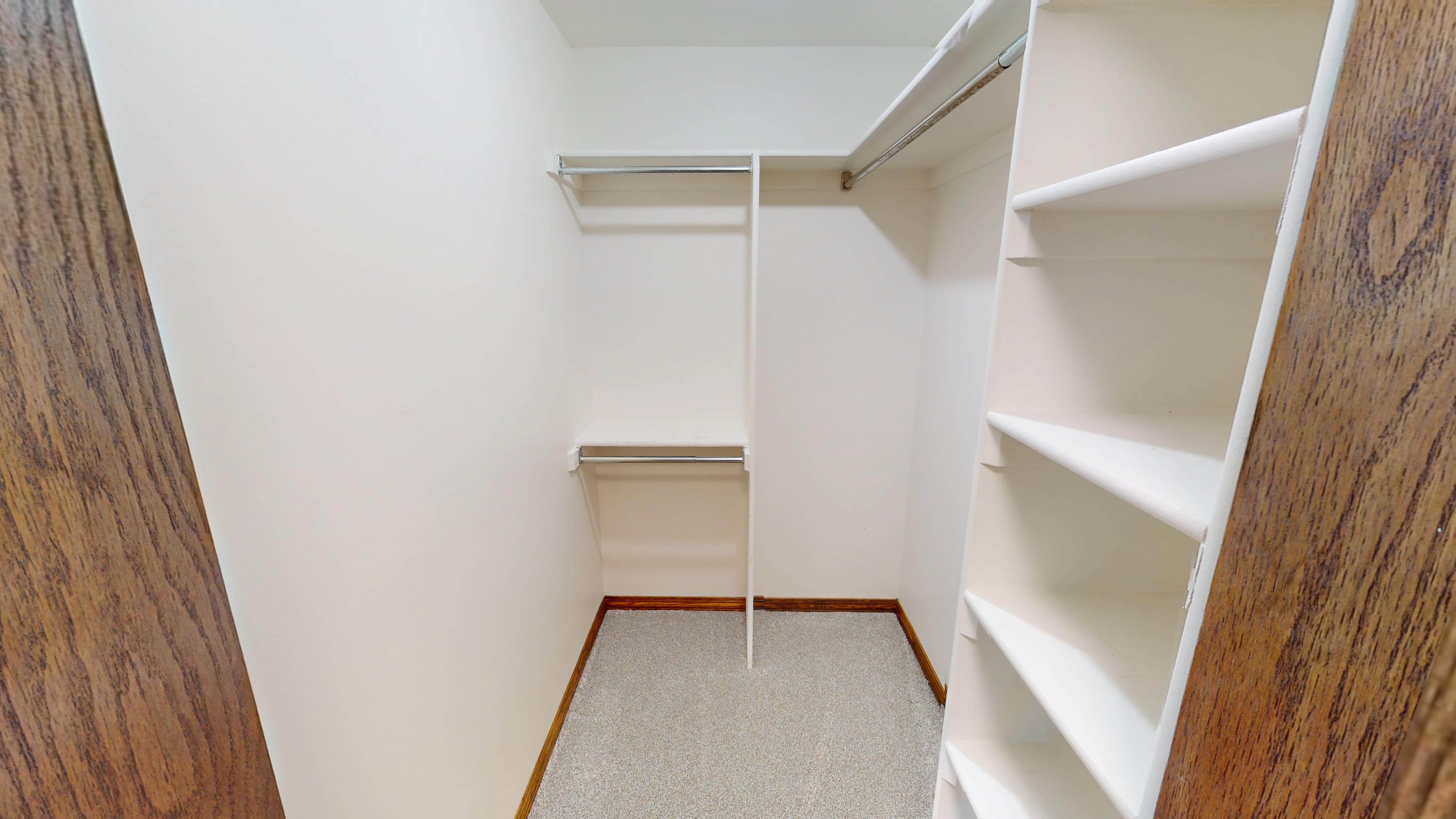 Walk-in closet featuring light-toned carpeting, white shelving units, and dual metal hanging rods