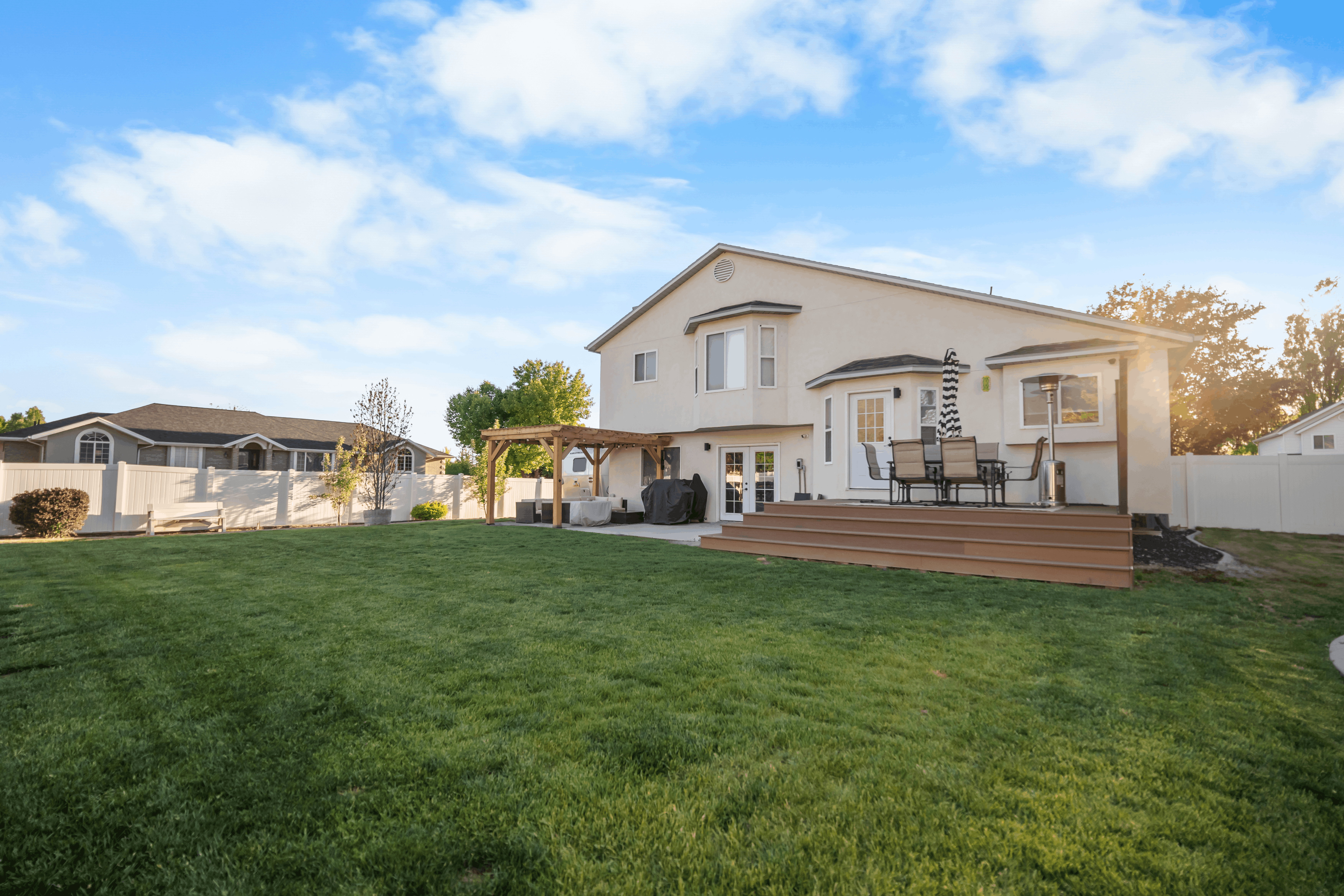 Expansive rear yard featuring a large composite deck, mature green lawn, and a light-colored privacy fence