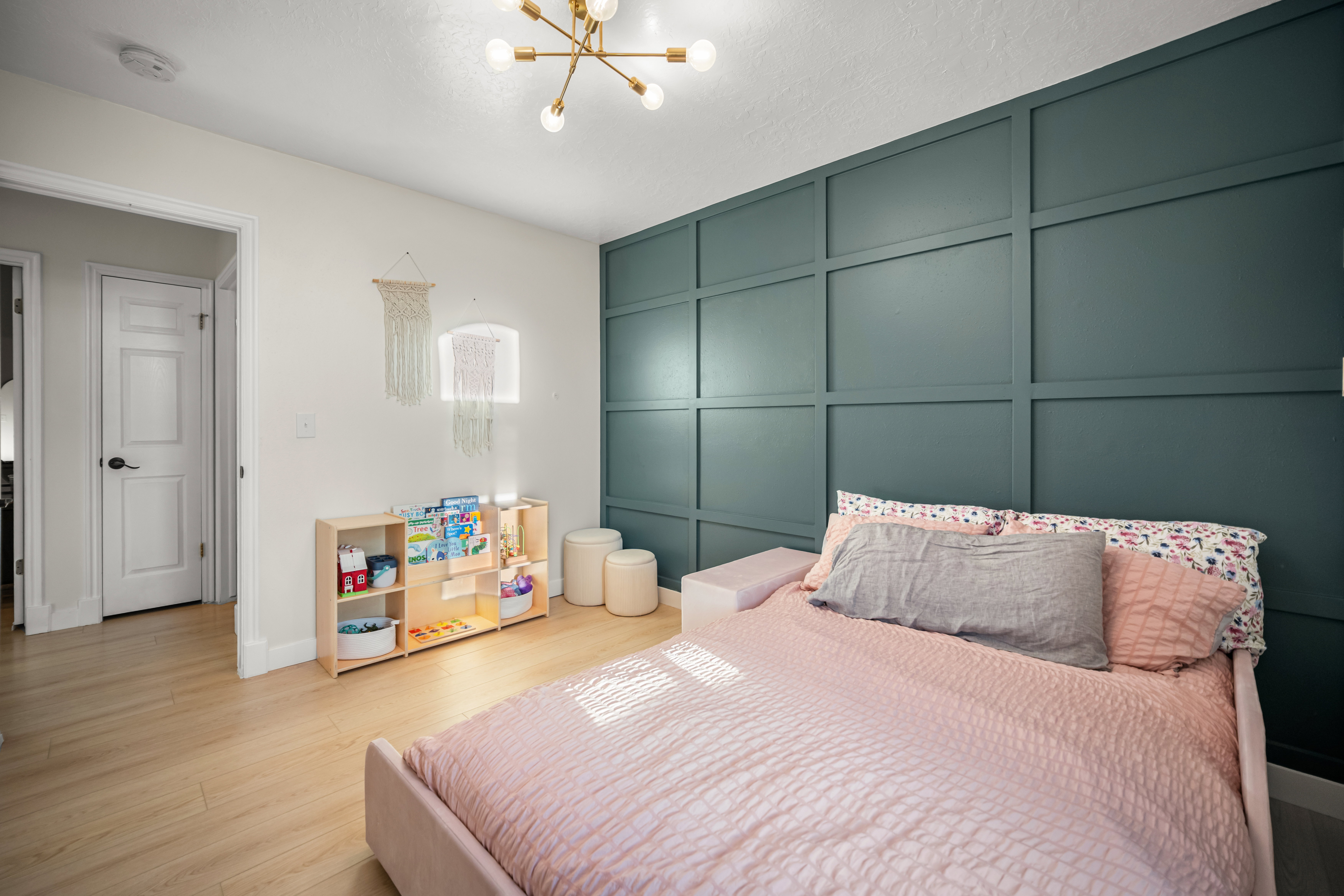 Bedroom featuring an accent wall with wainscoting, light wood-finish flooring, a contemporary sputnik chandelier, and a white interior door with black hardware