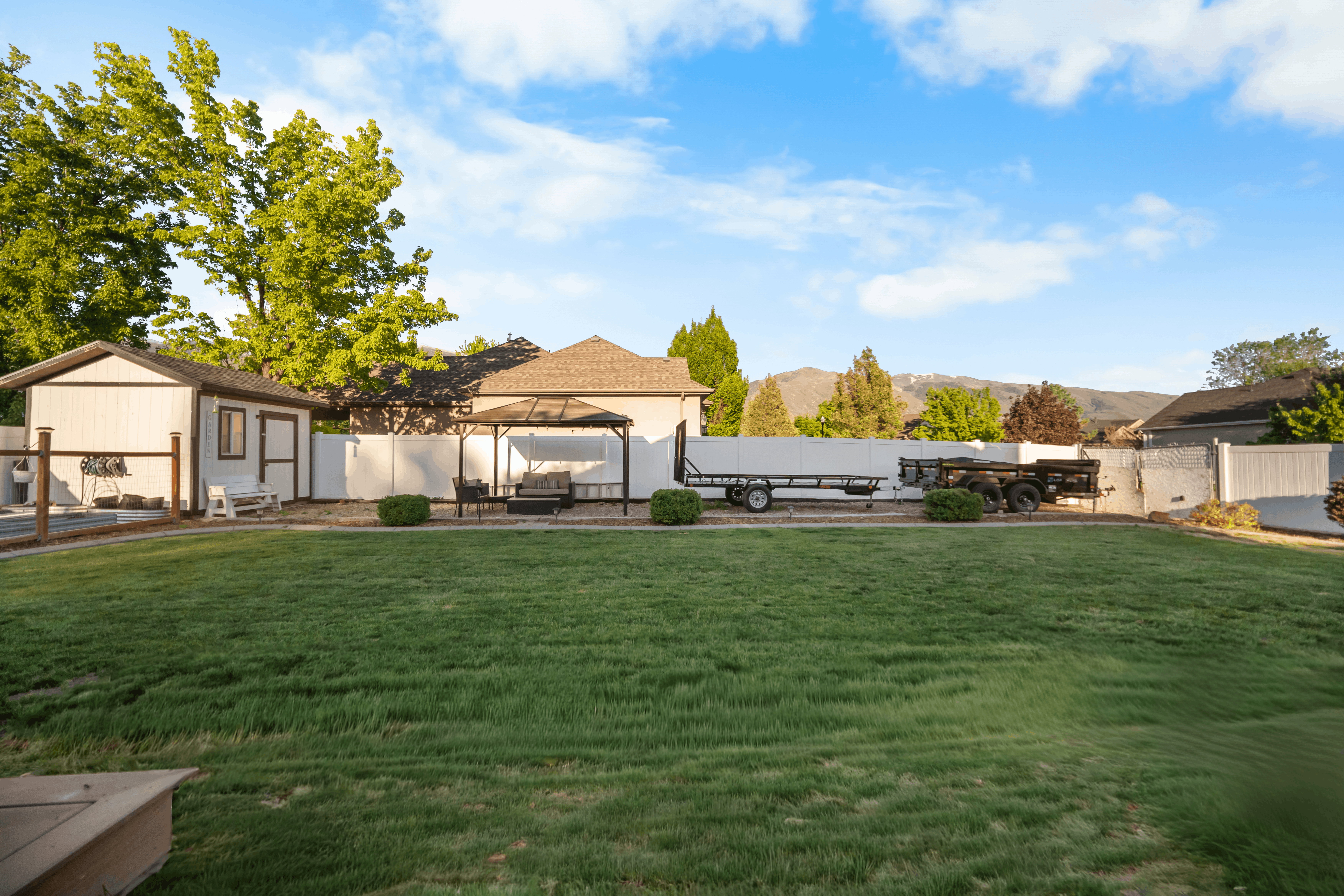 Spacious backyard featuring a manicured lawn, white privacy fencing, and a dedicated storage shed