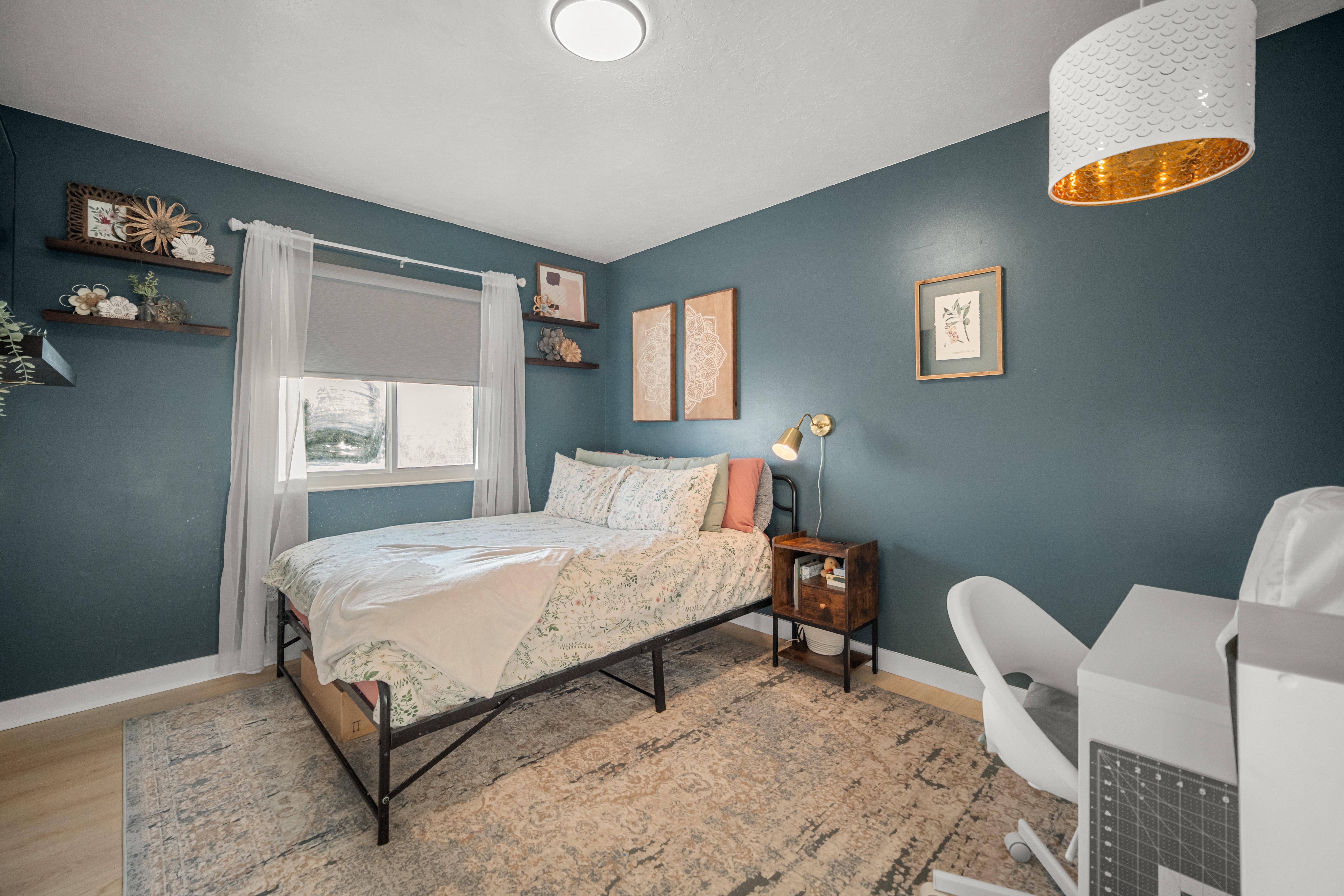 Room featuring wood-finish flooring, a window with roller shade and sheer curtains, an overhead drum pendant light with gold interior, and flush-mount ceiling lighting
