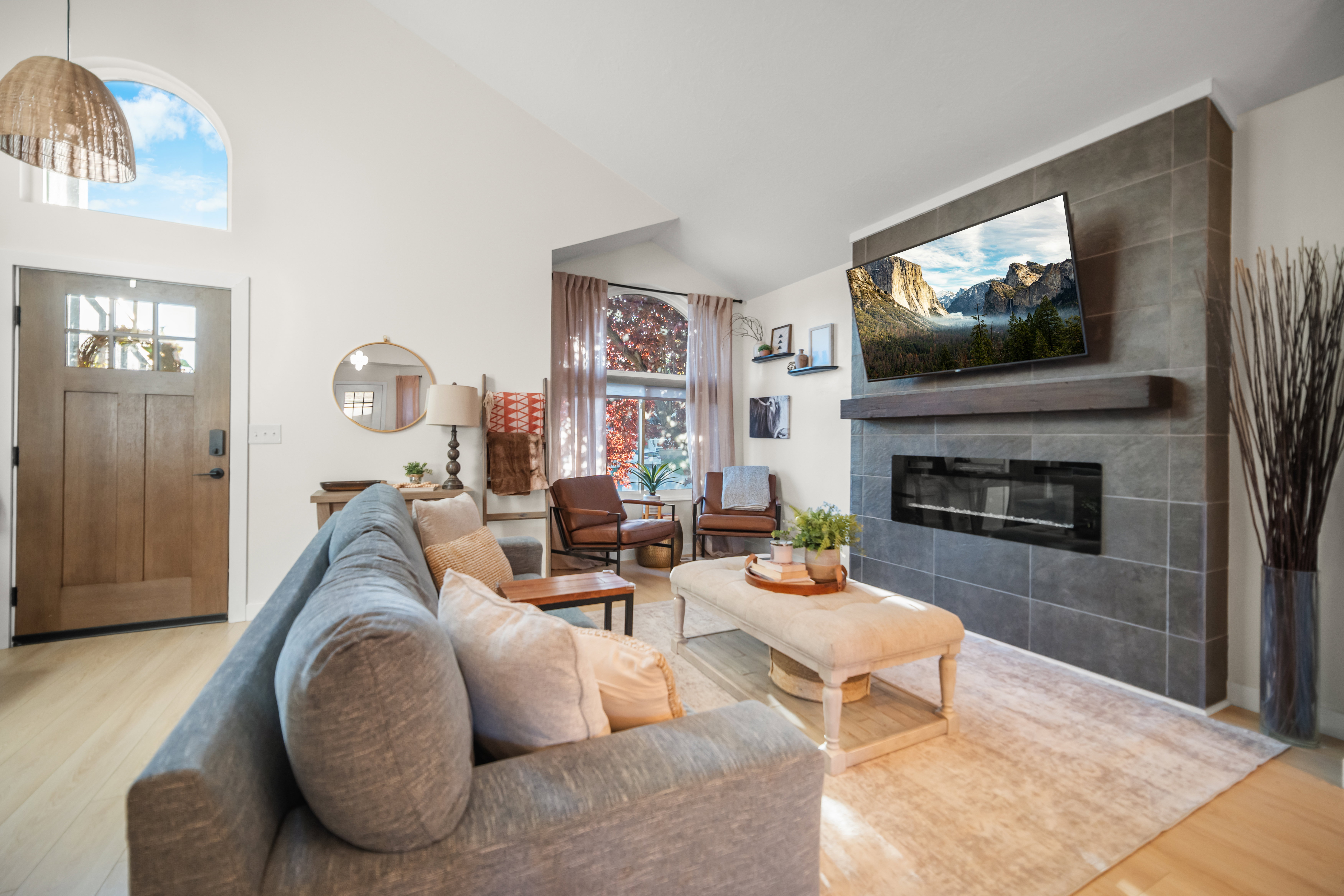 Living area featuring vaulted ceilings, light wood-finish flooring, and a contemporary fireplace with a dark tile surround and integrated hearth