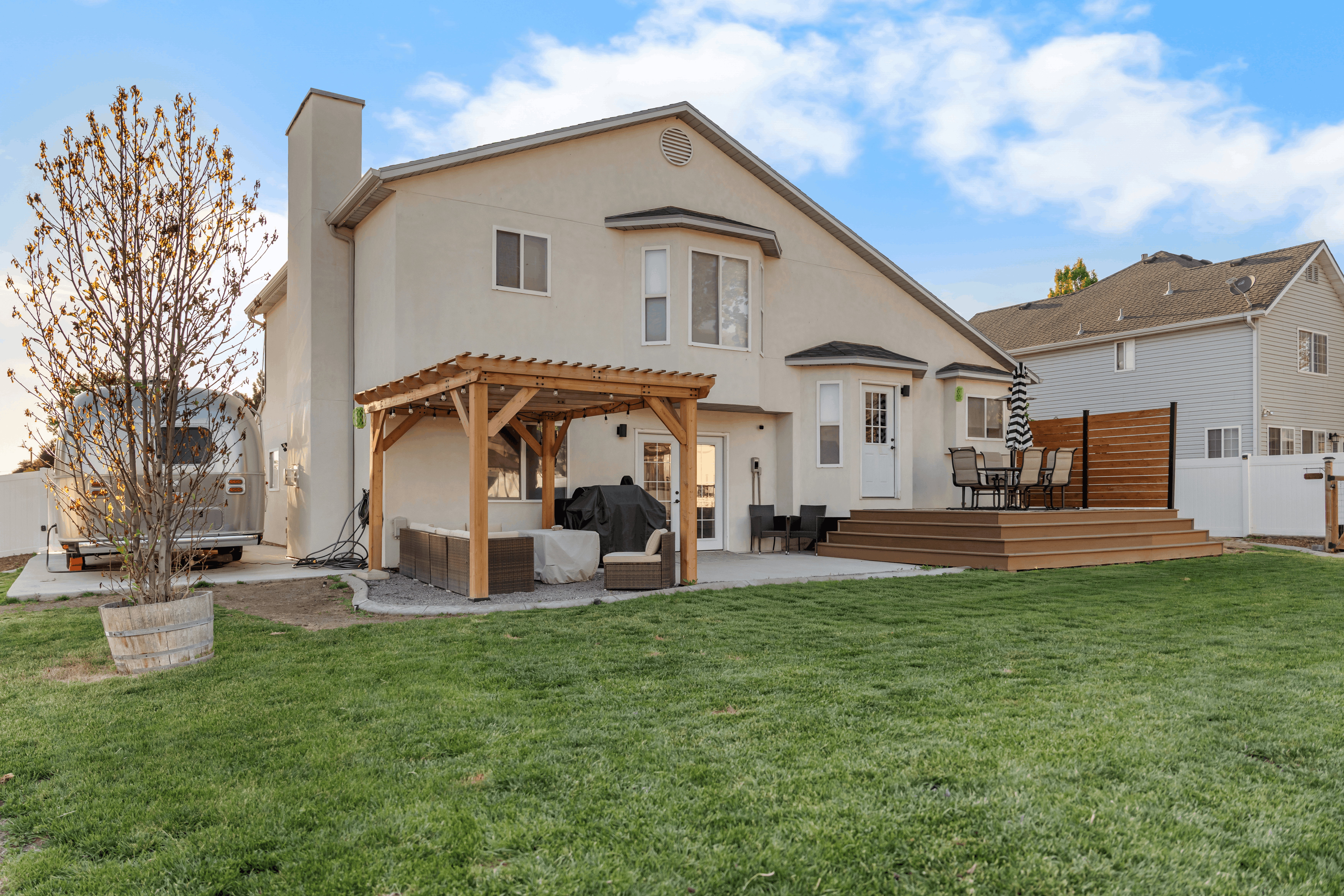 Expansive backyard featuring a manicured lawn, a large multi-level deck, a concrete patio, a wooden pergola, and a white vinyl fence