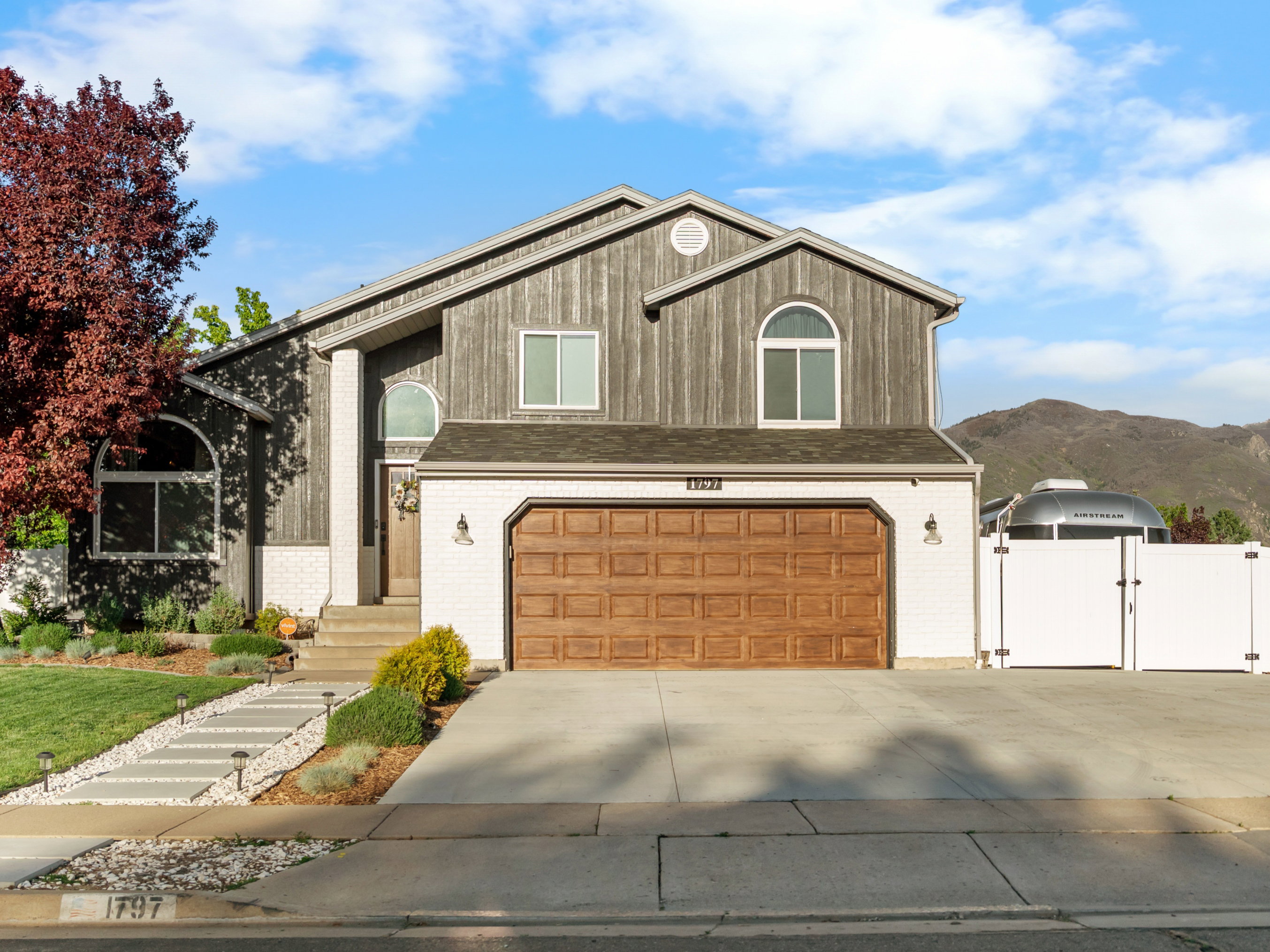 Contemporary two-story exterior featuring a prominent wood-finish garage door, a white privacy fence, and a front yard with a concrete walkway