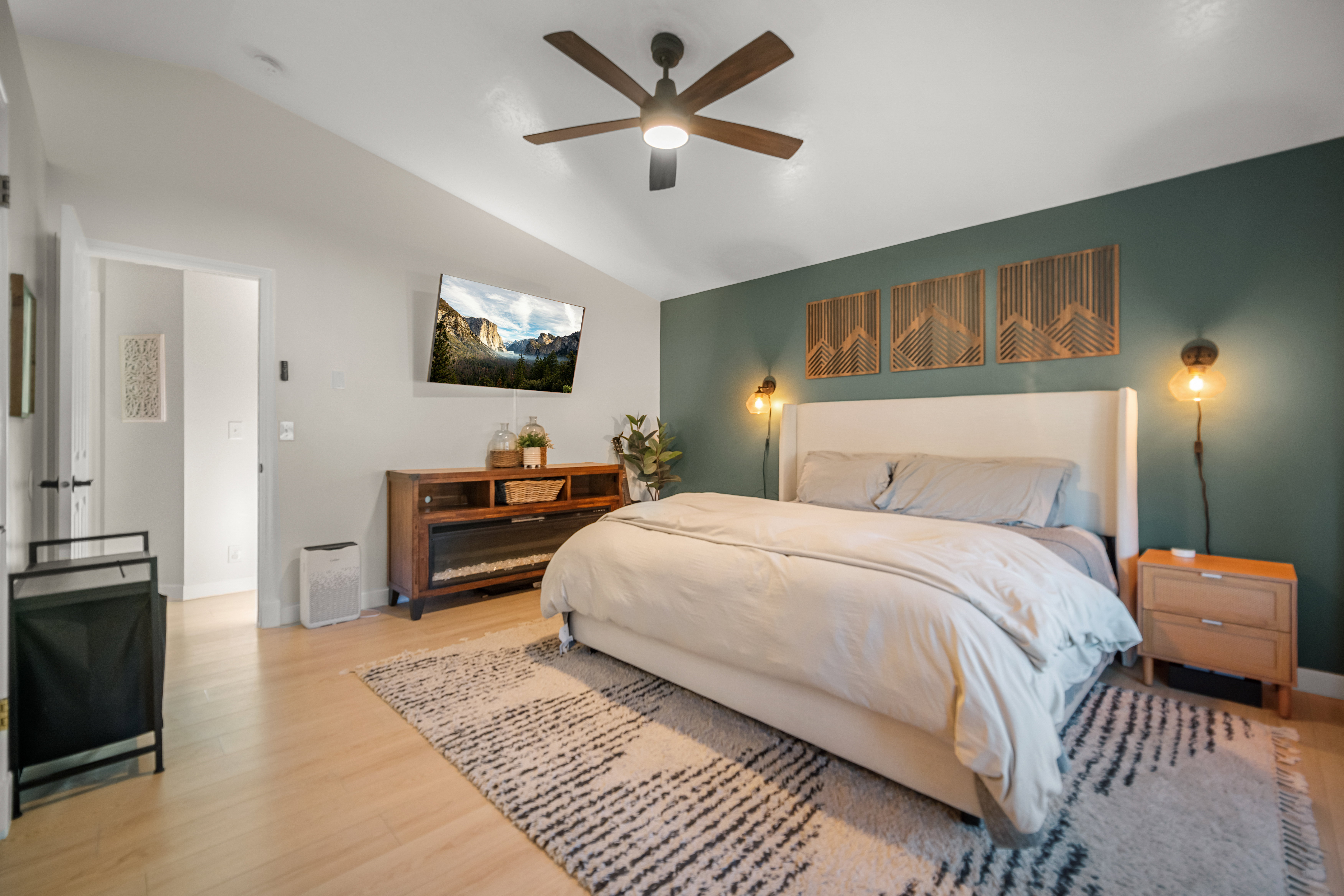 Spacious bedroom featuring vaulted ceilings, light wood-finish flooring, a contemporary ceiling fan, and a striking accent wall with integrated sconce lighting