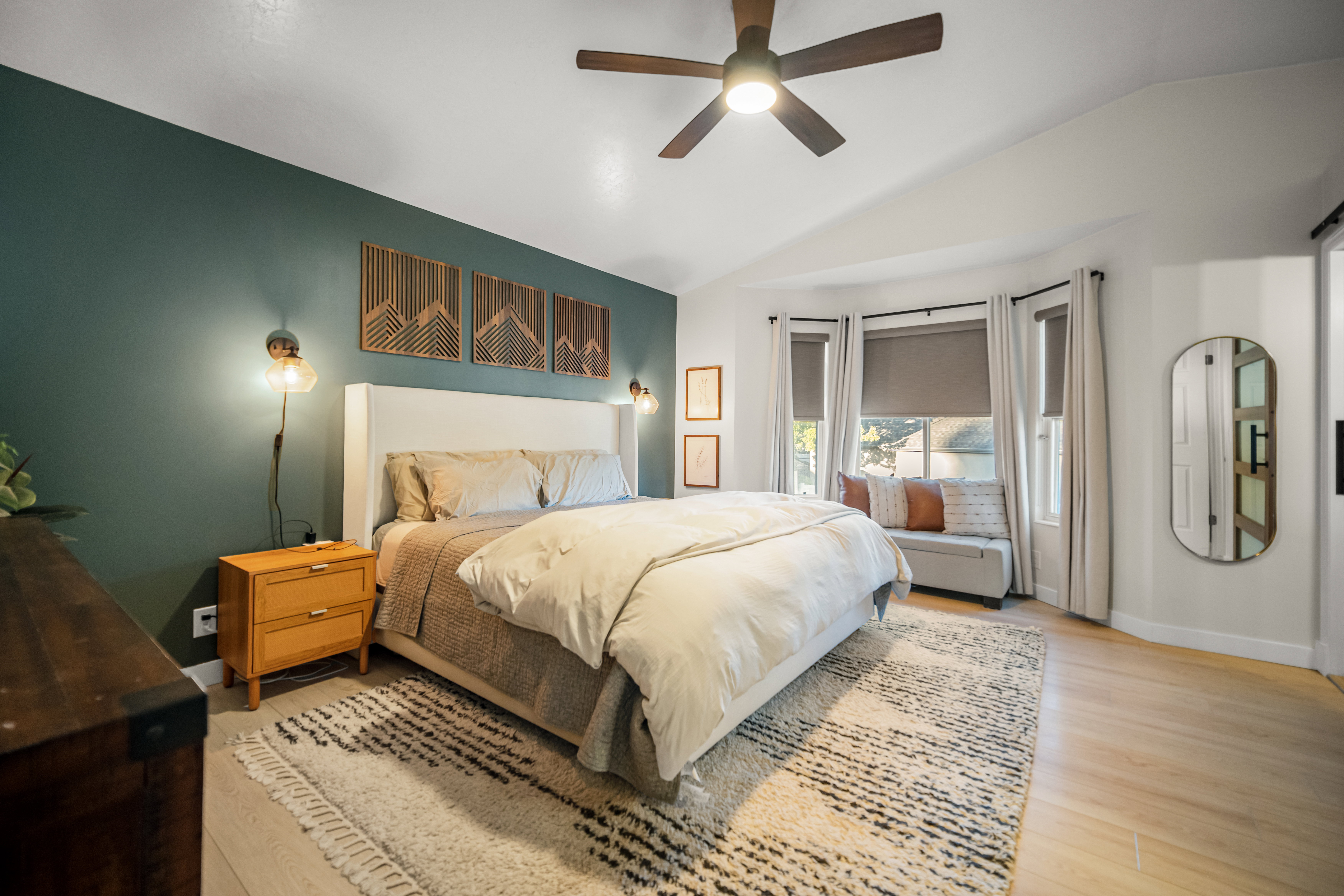 Spacious room featuring a bay window, wood-finish flooring, ceiling fan, and decorative wall sconces