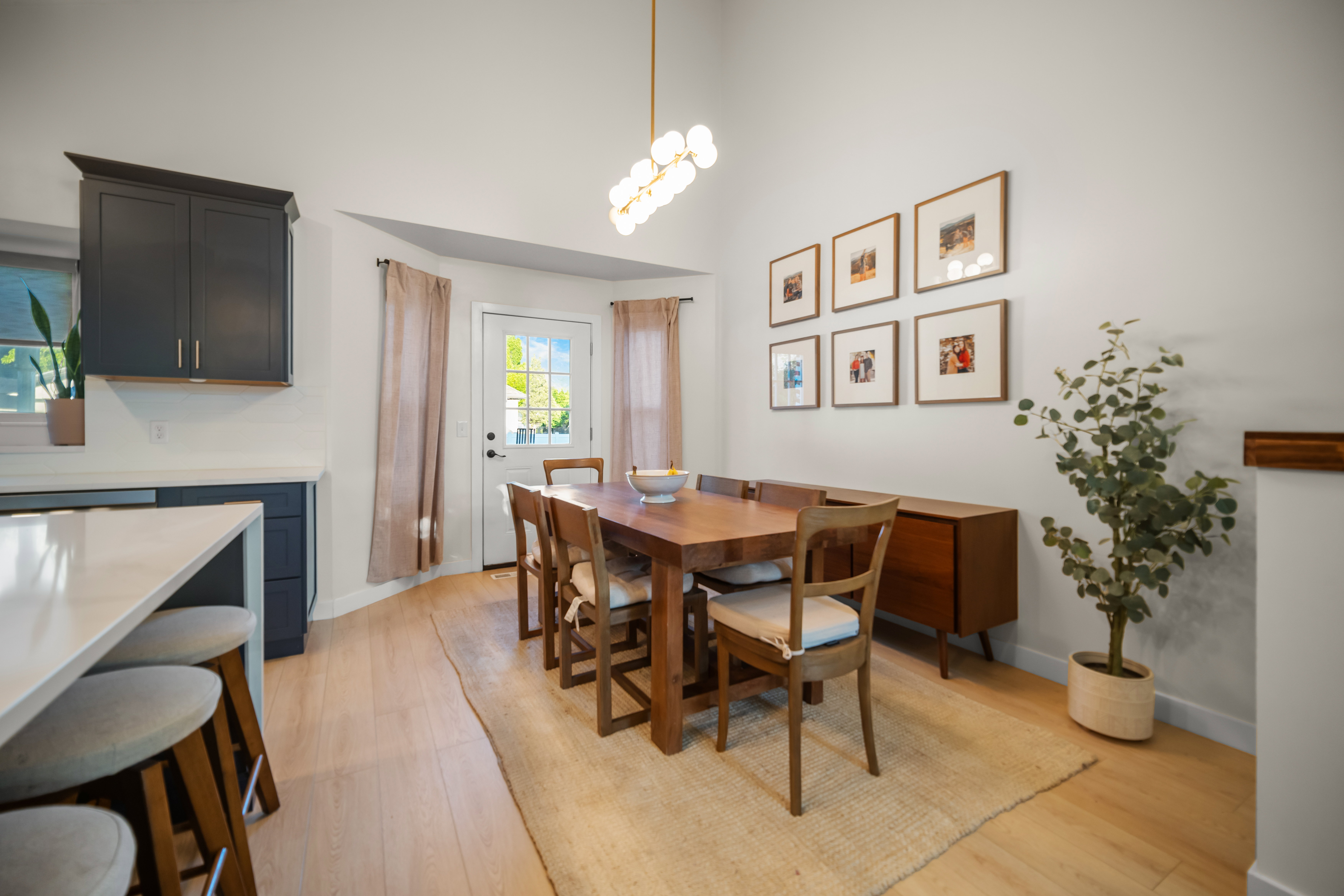 Dining area featuring vaulted ceilings, light wood-finish flooring, a modern linear chandelier, and a glass-paneled door for exterior access