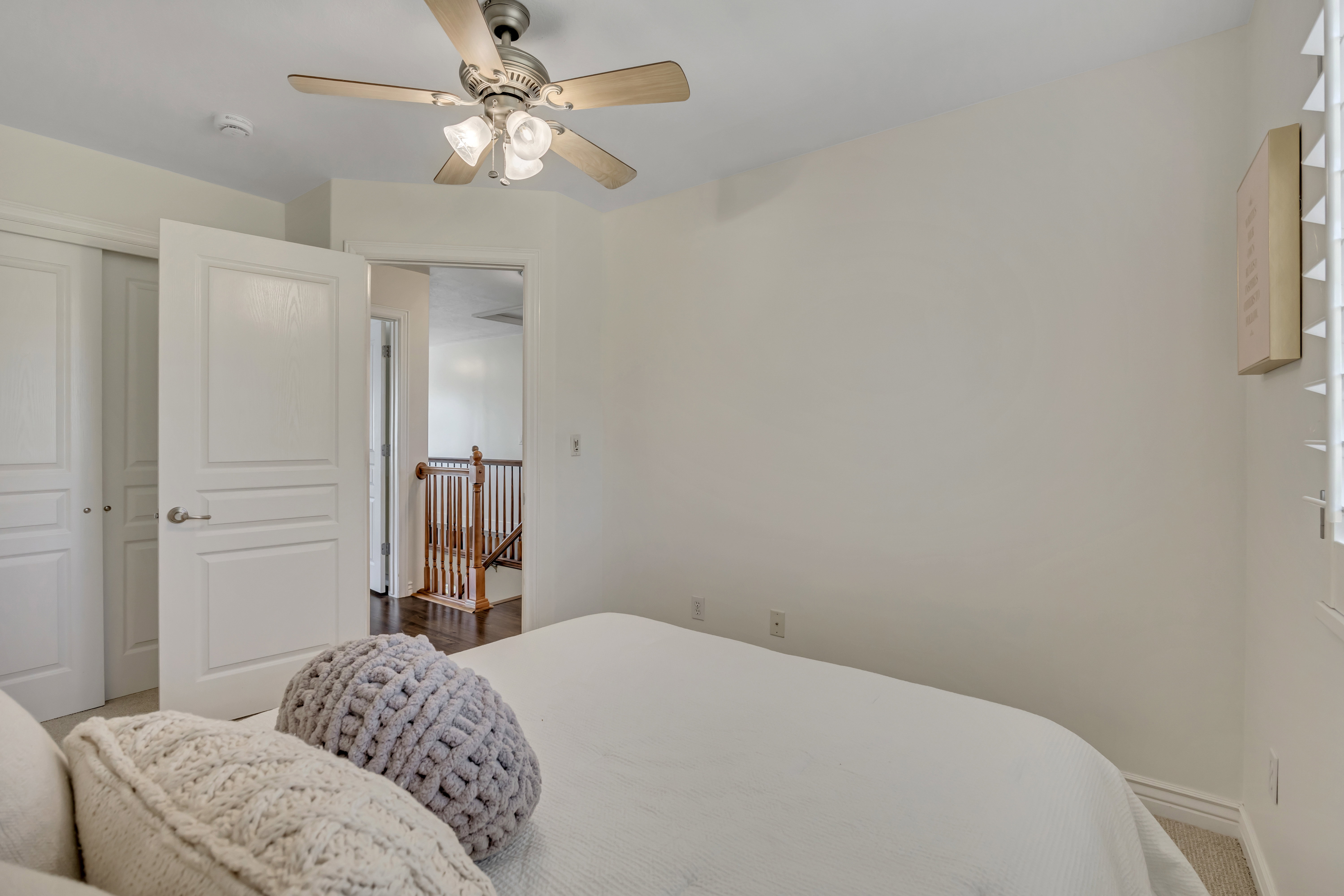 2nd upper level bedroom neutral wall finishes with a ceiling fan light fixture, white plantation shutters, and light-colored carpeting