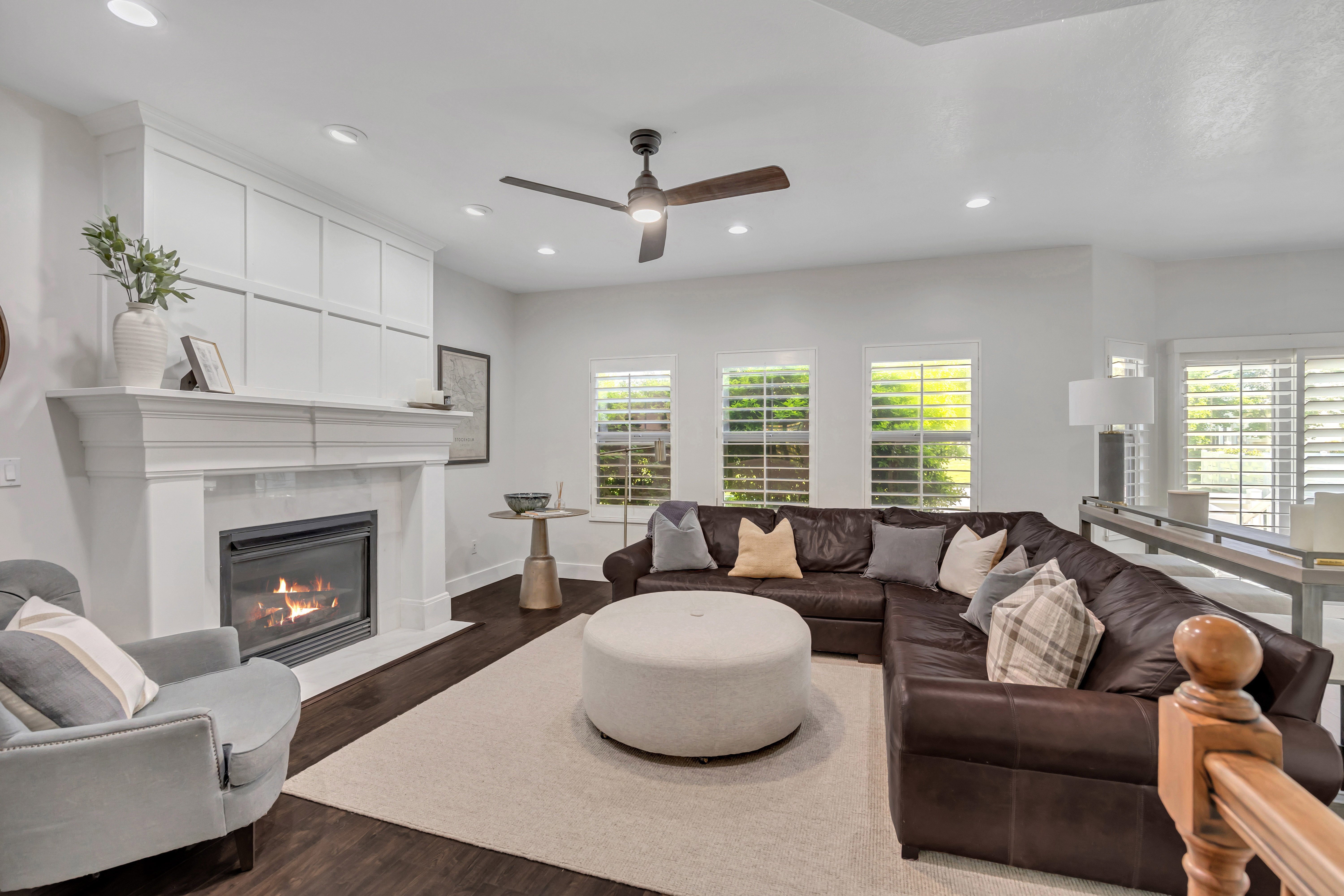 Living area featuring a fireplace with a white mantel, recessed lighting, ceiling fan, wood-finish flooring, and multiple windows with plantation shutters