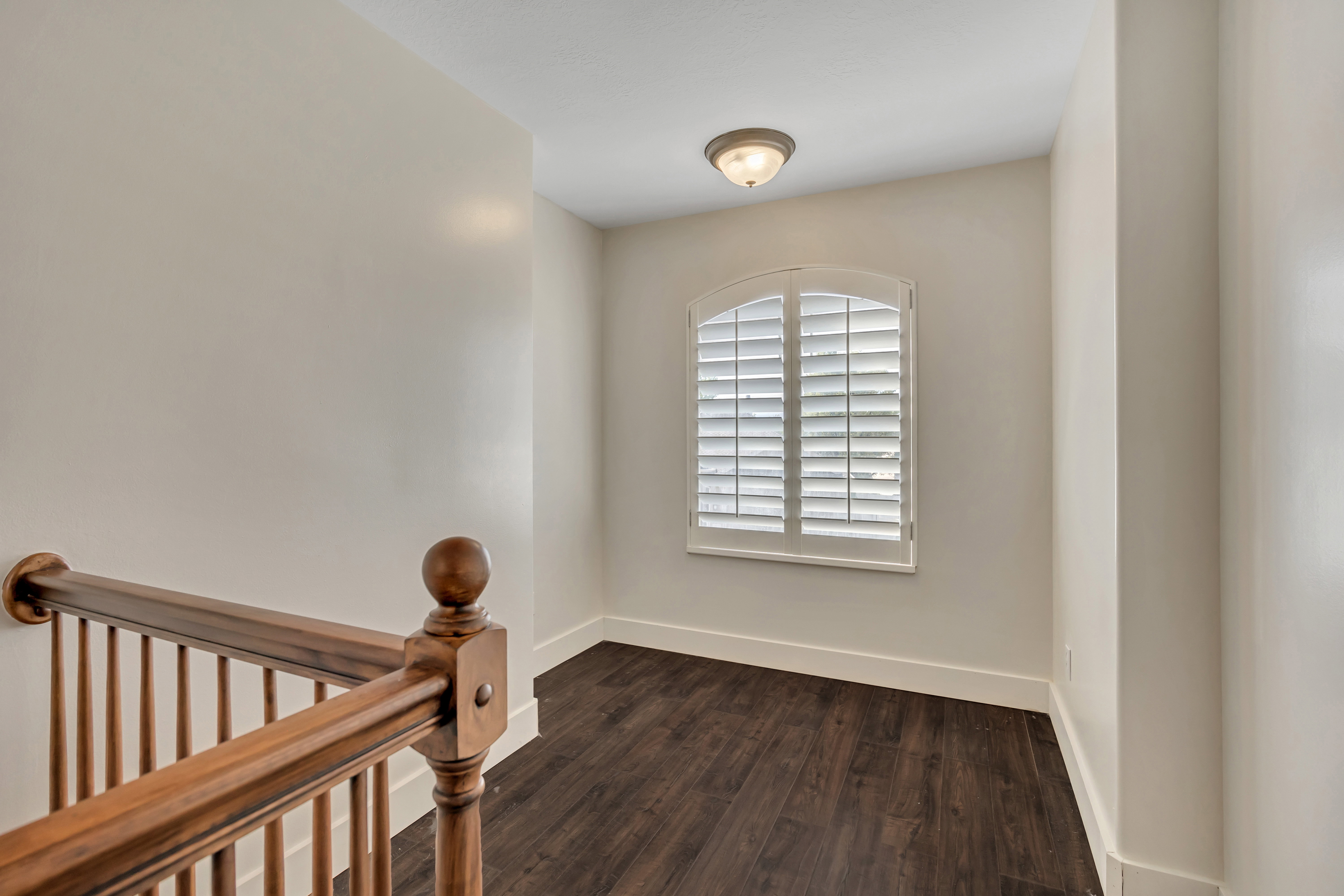 Bonus Room Arched window with white plantation shutters, dark wood-finish flooring, and a flush mount ceiling light