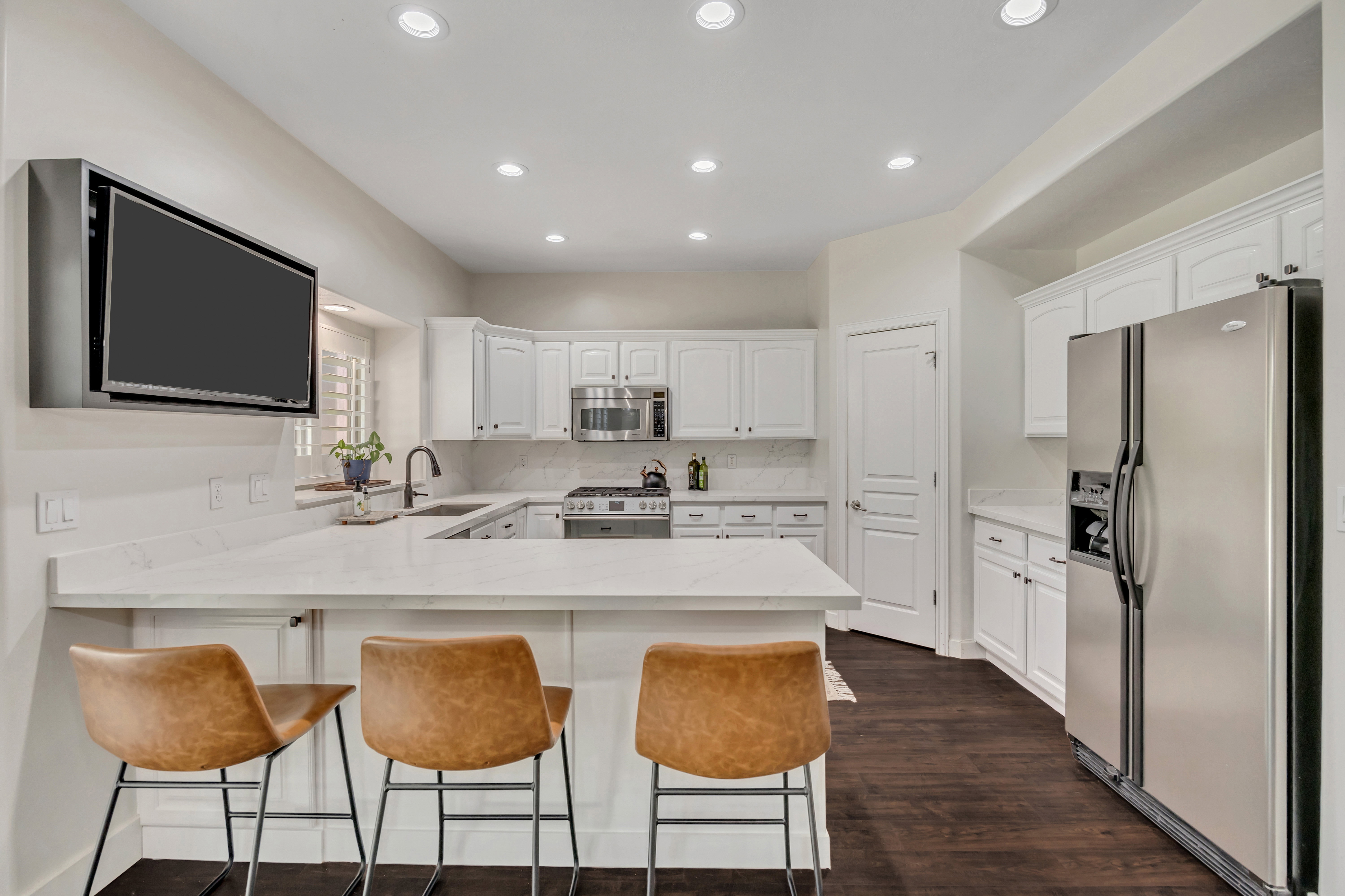 Modern kitchen featuring white cabinetry, light countertops, wood-finish flooring, a stainless steel refrigerator, and recessed lighting