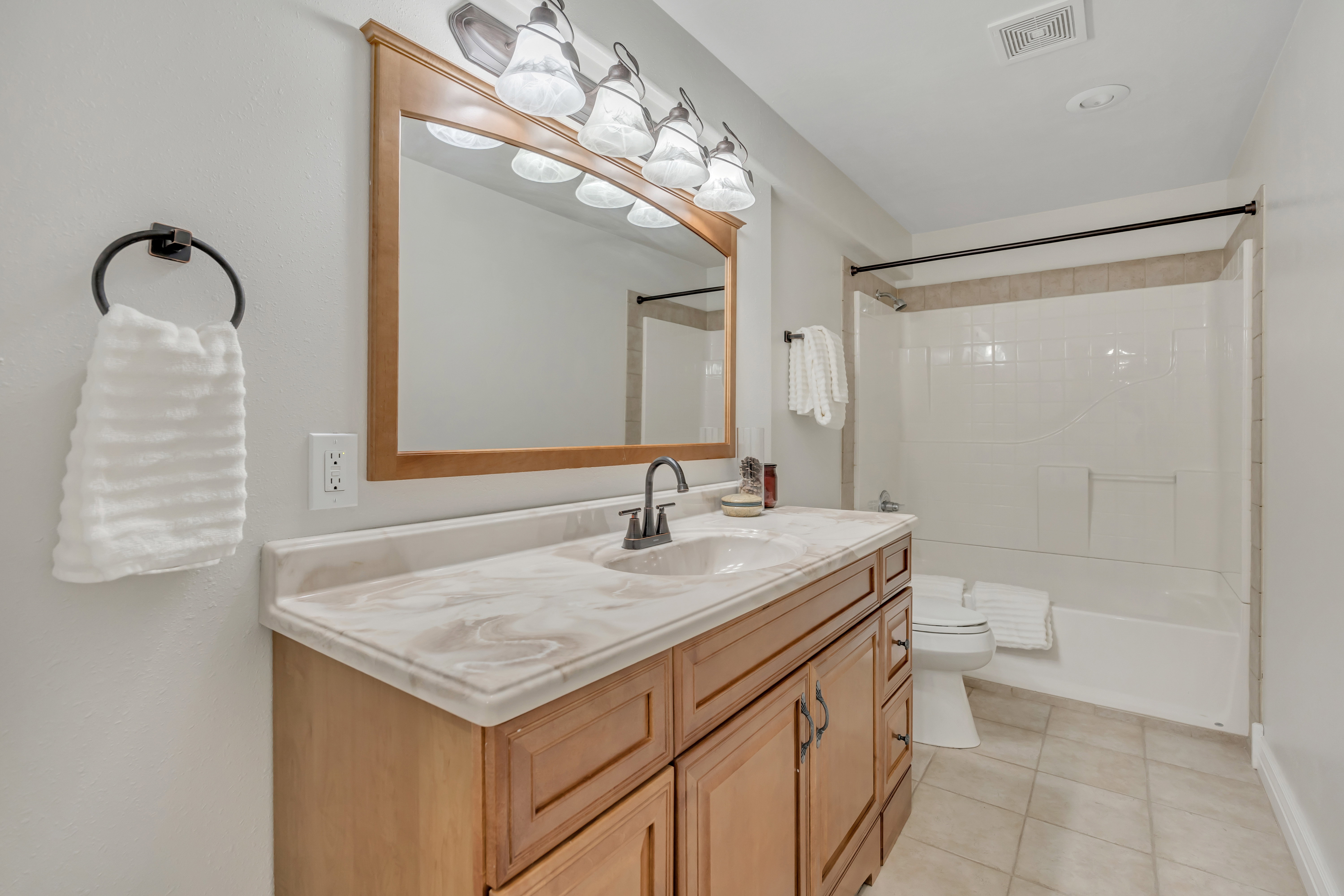Bathroom featuring a wood-finish vanity with a light-colored countertop, an undermount sink, and a framed mirror with overhead lighting