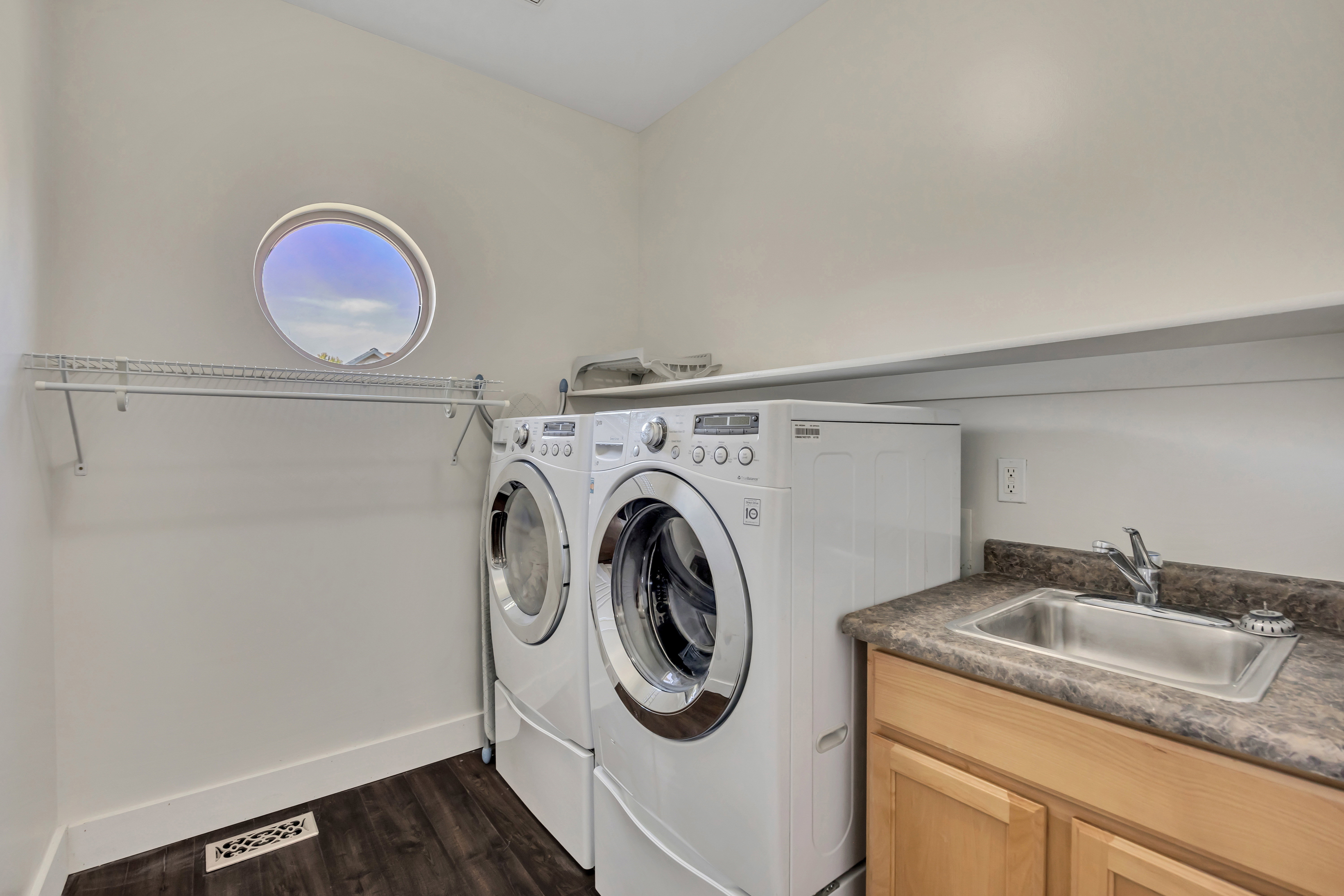 Laundry area featuring a round porthole window, wood-finish flooring, and a utility sink with a base cabinet