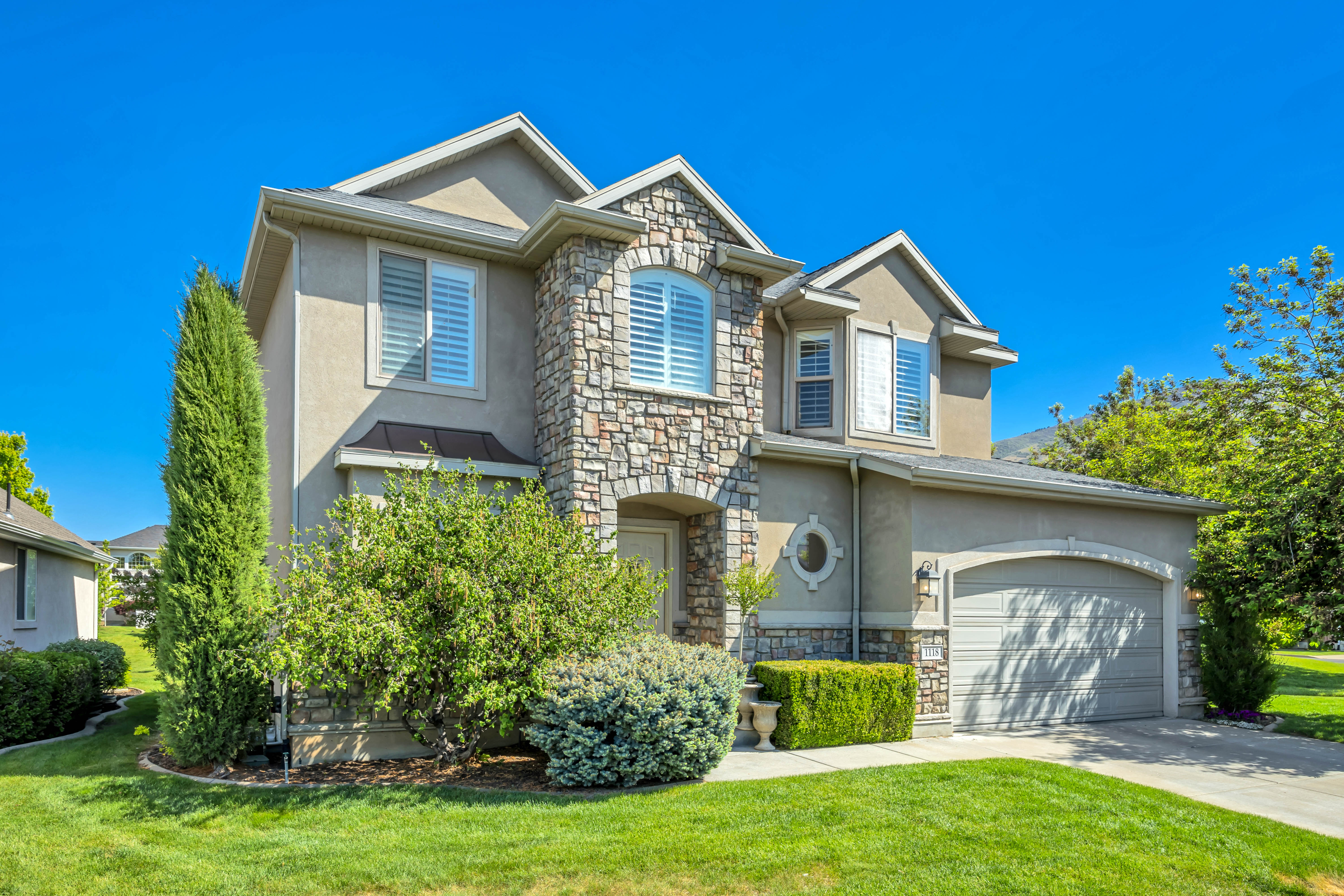 Stucco exterior featuring extensive stone accents, a two-car garage, manicured landscaping, and arched window details