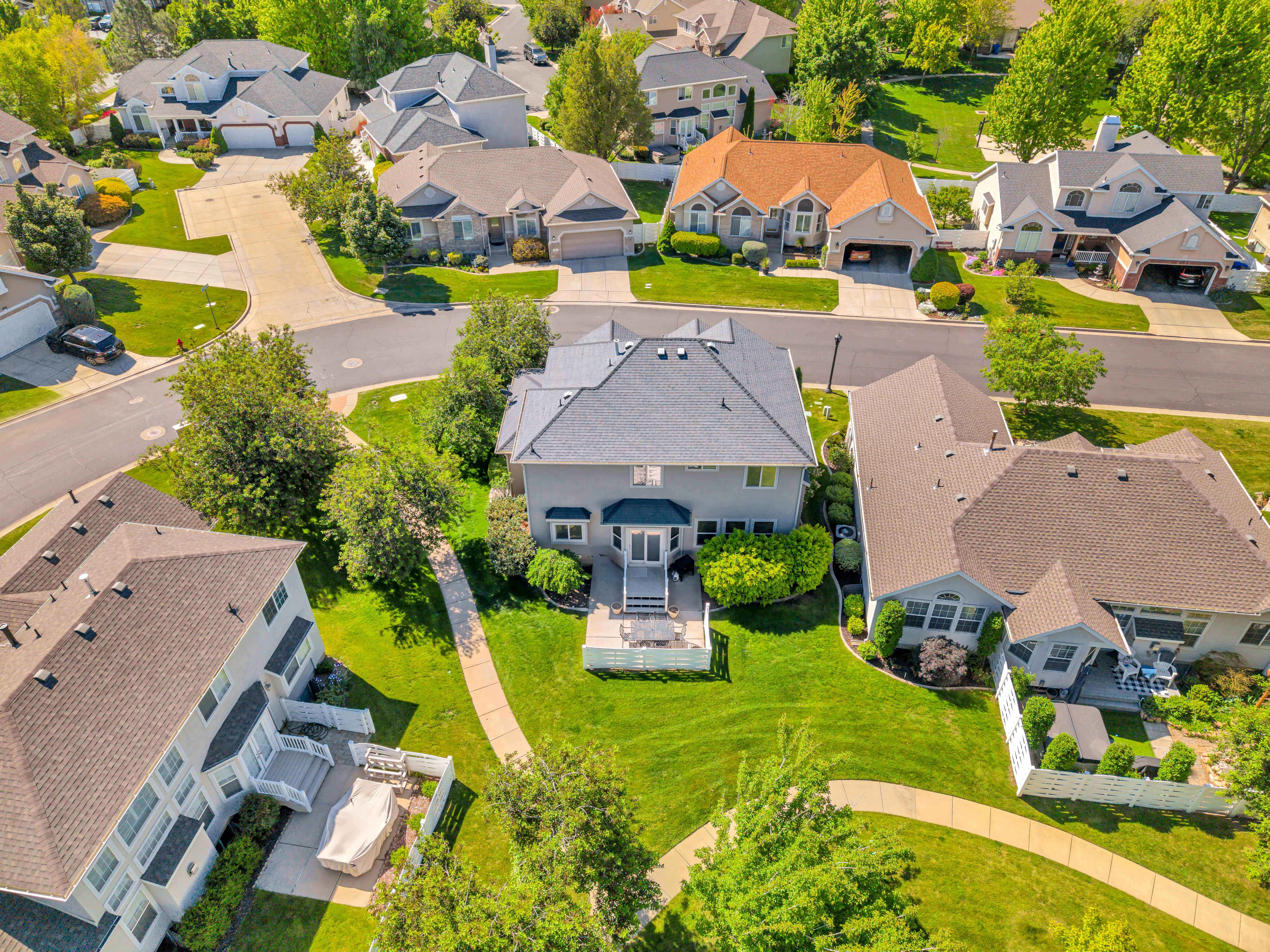Aerial perspective showcasing a residential property with a multi-level deck, surrounding green landscaping, and paved pathways