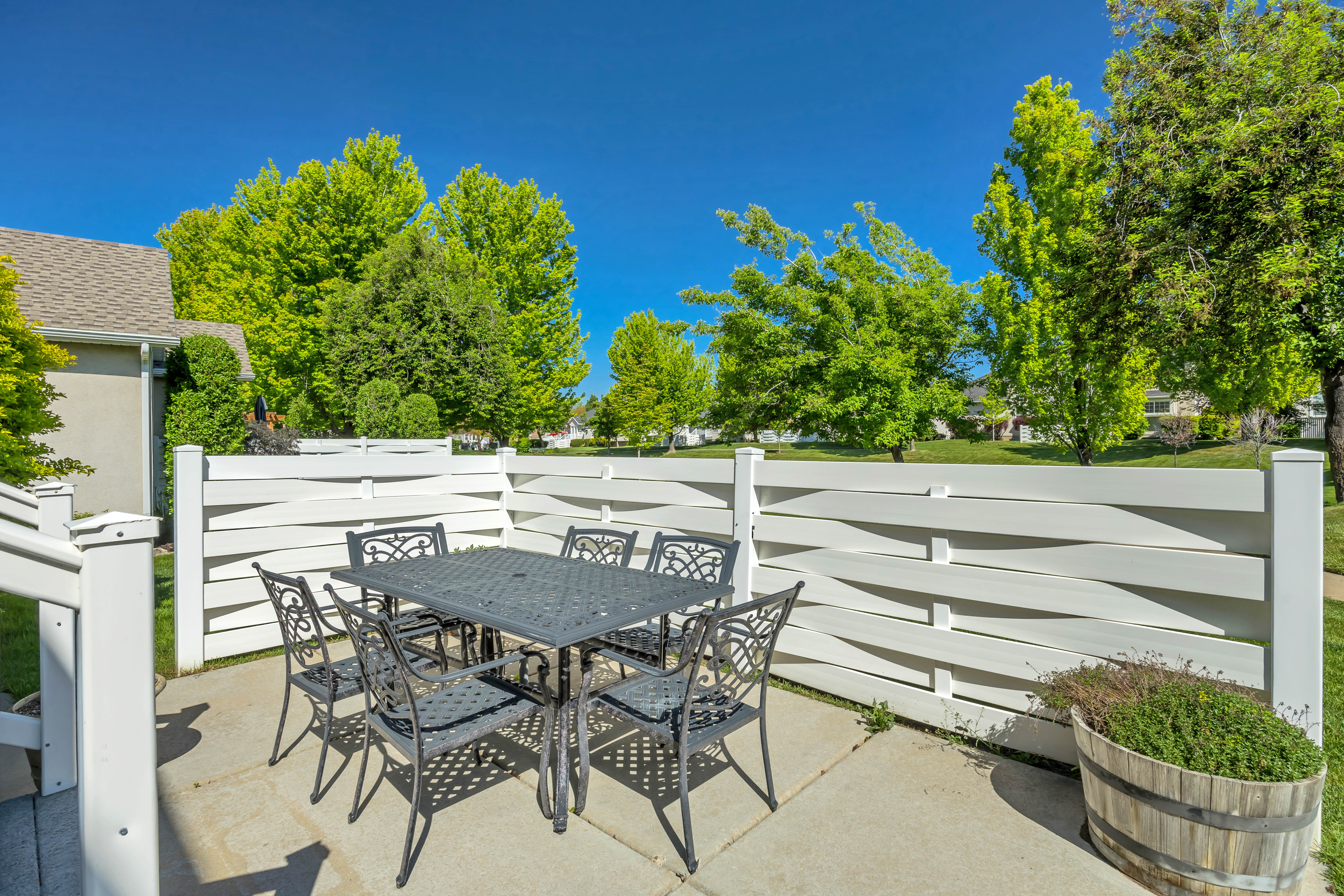 Concrete patio featuring a decorative white fence, mature trees, and a barrel planter