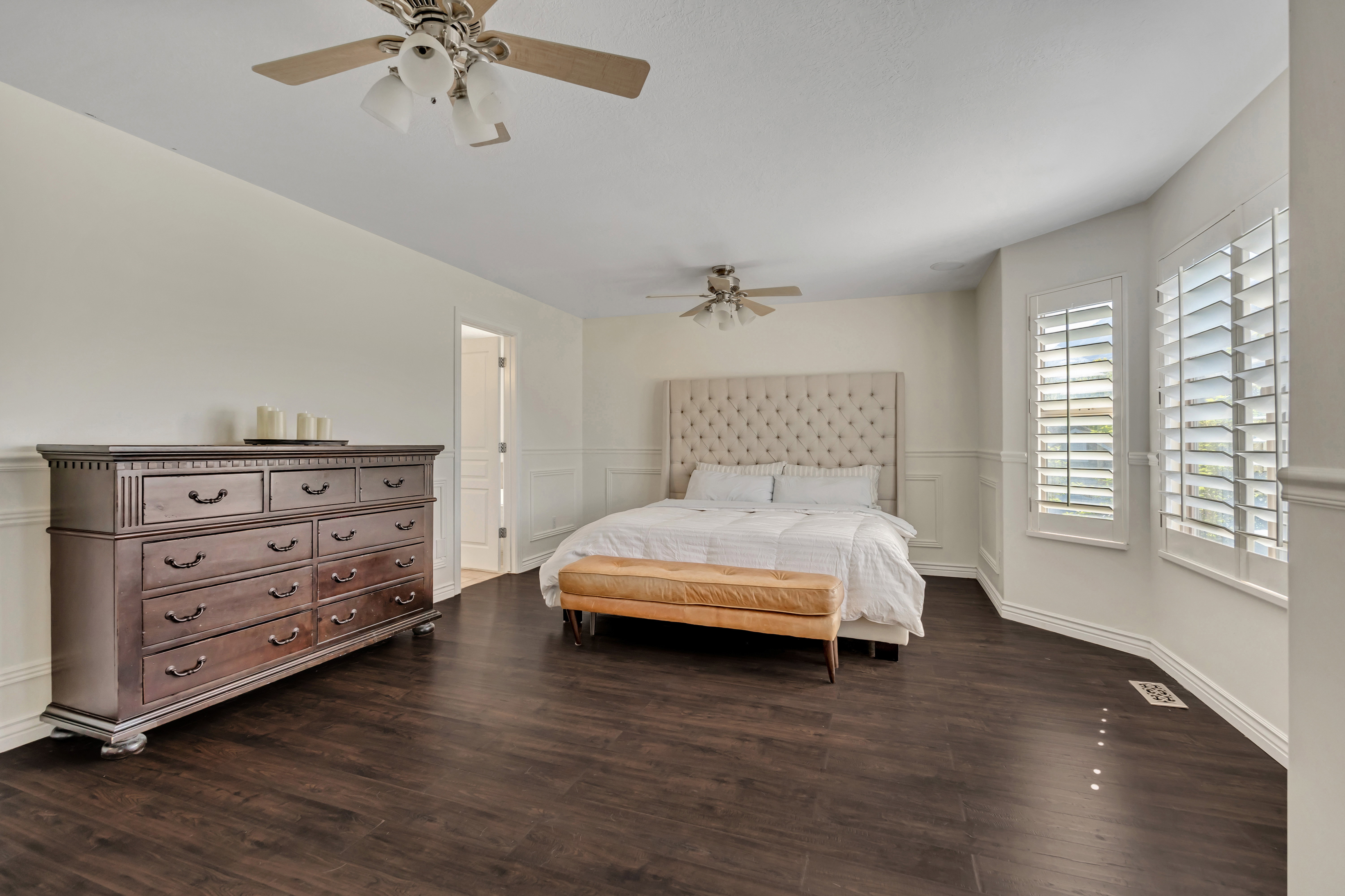 Spacious room featuring wood-finish flooring, two ceiling fans with integrated lighting, and neutral wall tones
