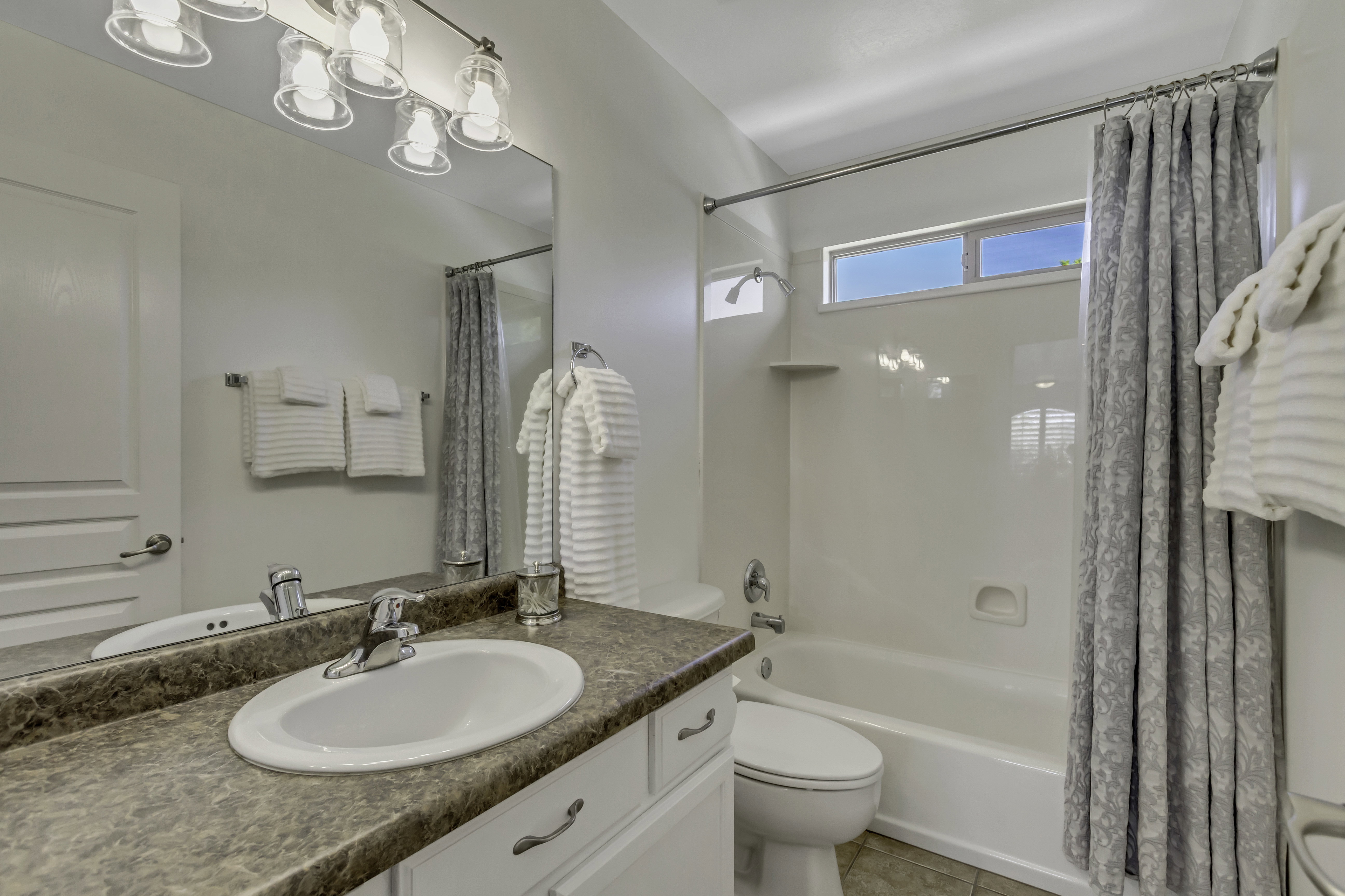 Upper level Full Bathroom with tile flooring, a white vanity with solid surface countertop, a built-in tub with shower.