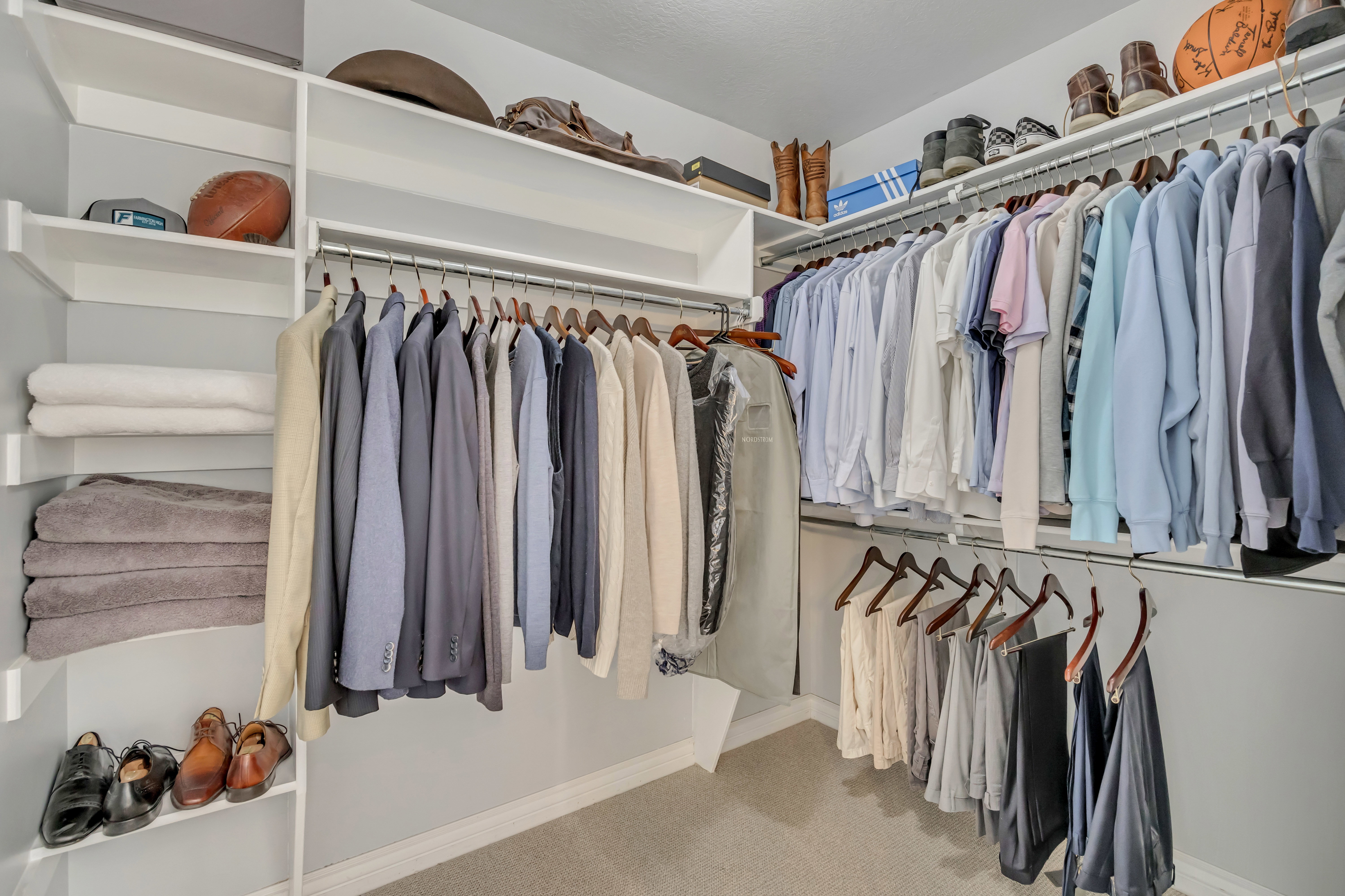 Walk-in closet system featuring multiple hanging rods, white shelving, and carpet flooring