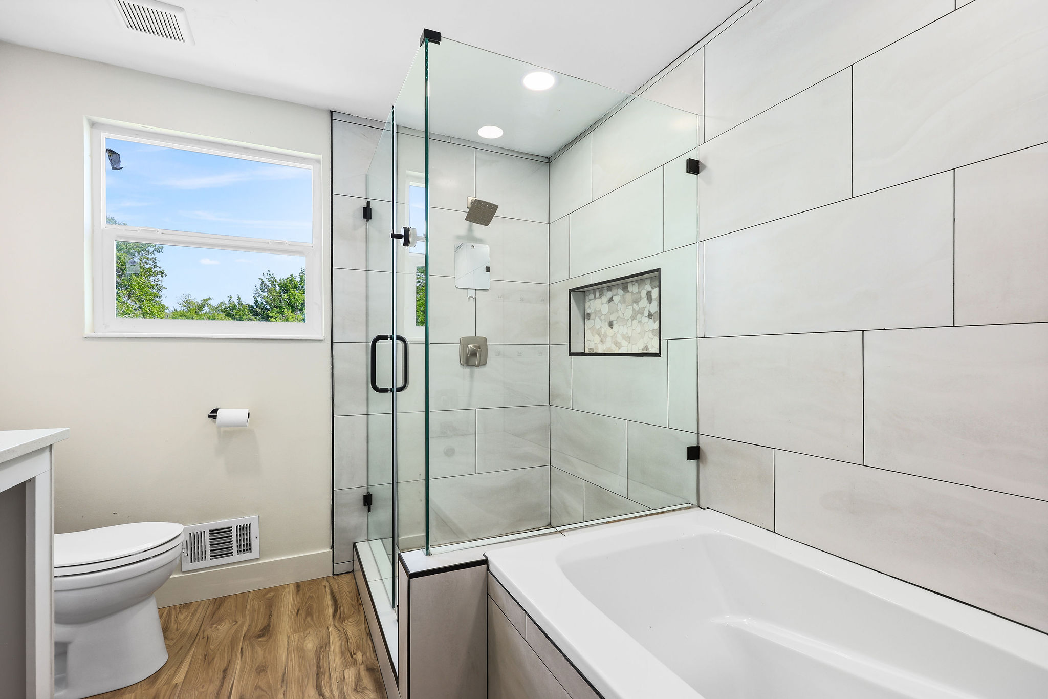 Modern bathroom featuring a glass-enclosed shower, built-in shower niche with mosaic tile, a separate soaking tub, and wood-finish flooring