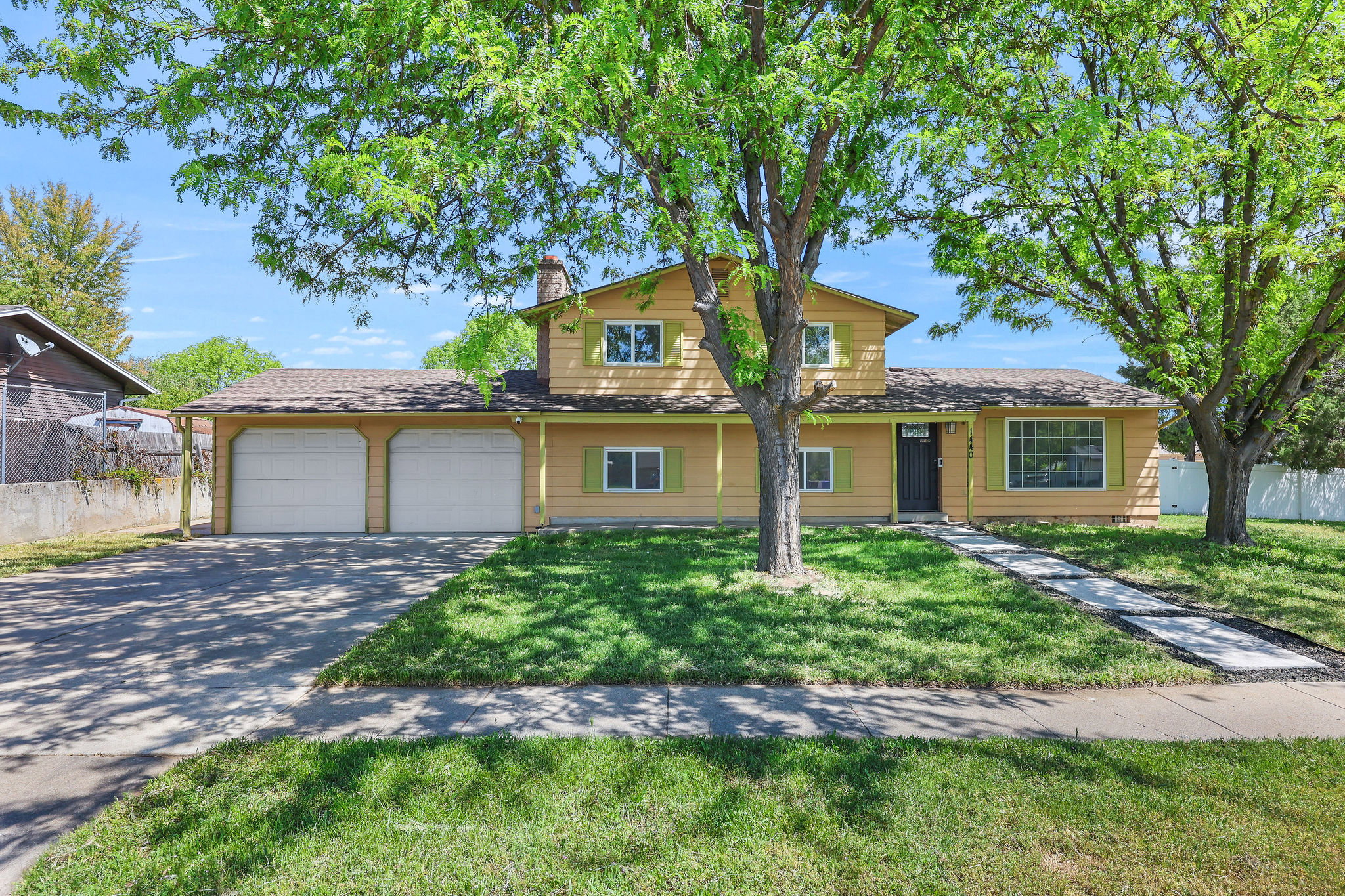 Split-level residence featuring a two-car garage with white doors, a yellow exterior with green shutters, and a dark entry door