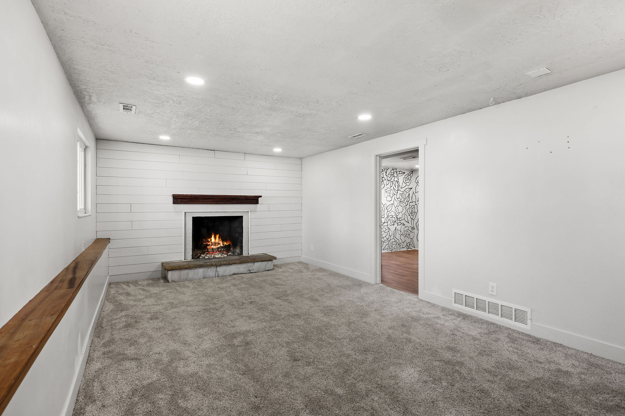 Living space with a white shiplap accent wall, fireplace with stone hearth, wood mantel, recessed lighting, and grey carpet flooring
