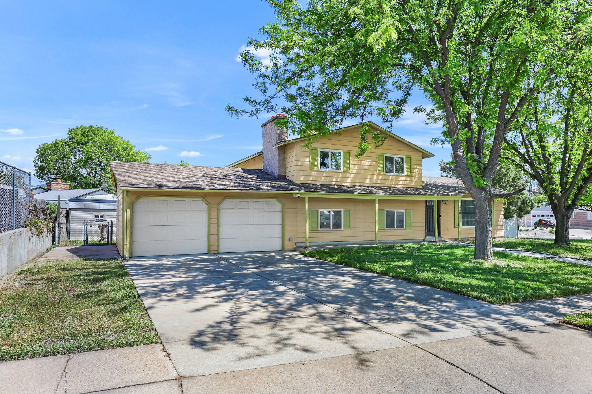 Yellow two-story residence featuring a two-car garage, covered porch entry, and light green decorative shutters