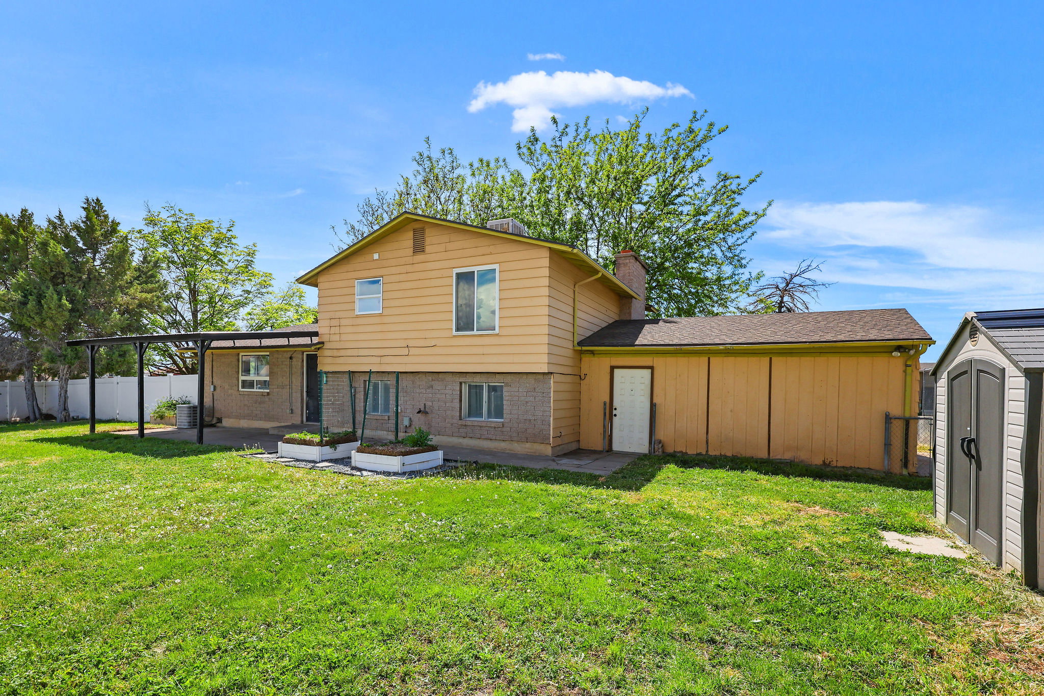 Expansive grass lawn featuring a covered patio, raised garden beds, and a storage shed