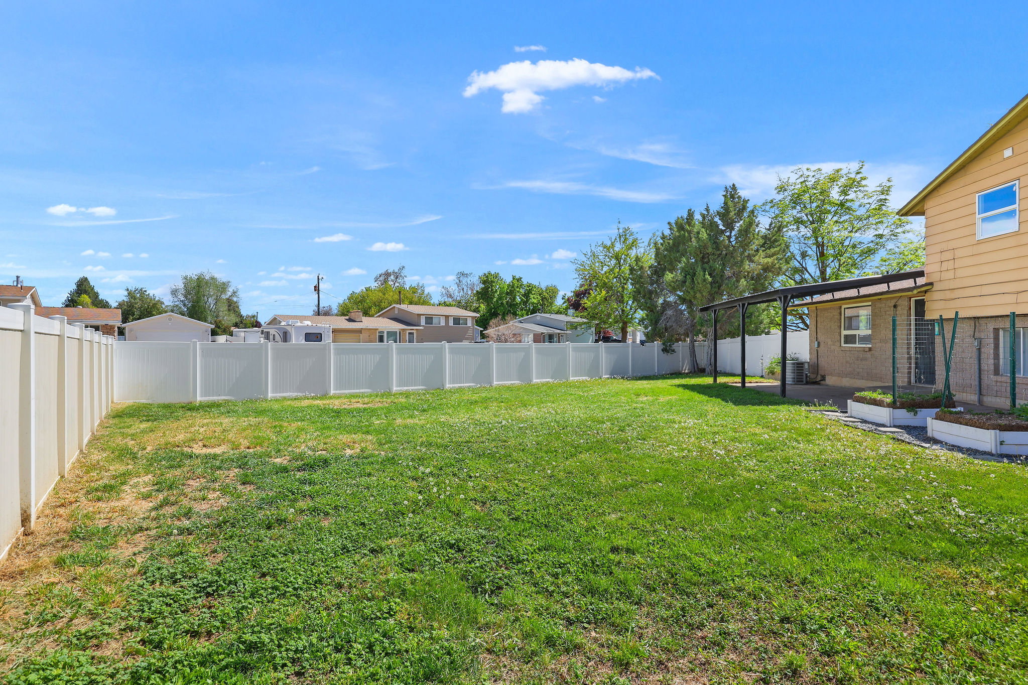 Expansive backyard featuring a manicured lawn, full vinyl privacy fencing, and a covered patio structure