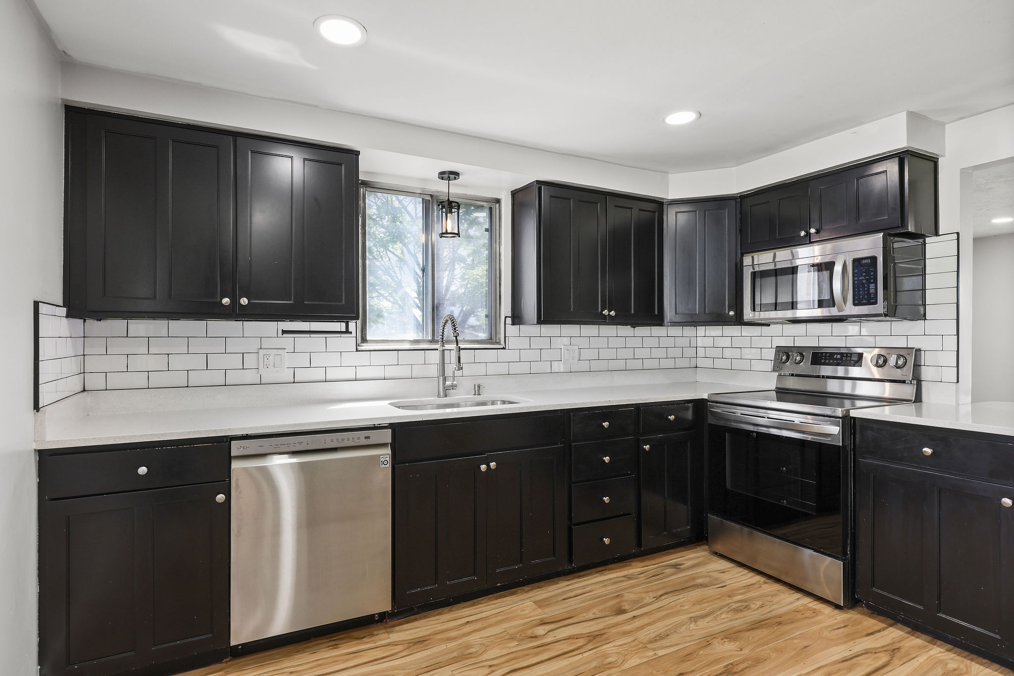 Modern kitchen featuring dark wood-finish cabinetry, stainless steel appliances, white subway tile backsplash, and light-toned countertops