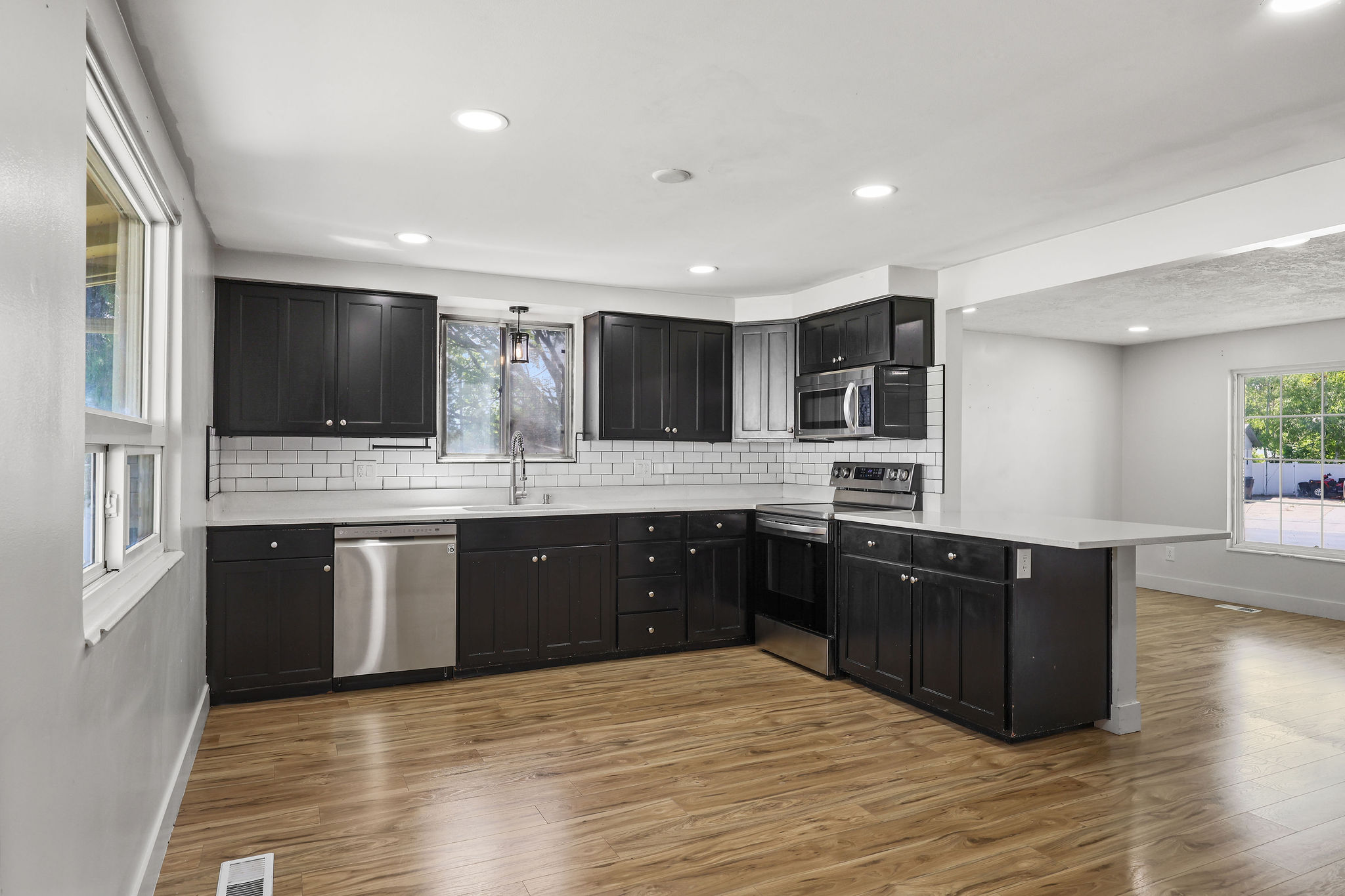 Modern kitchen featuring dark cabinetry, stainless steel appliances, a white subway tile backsplash, light countertops, and wood-finish flooring
