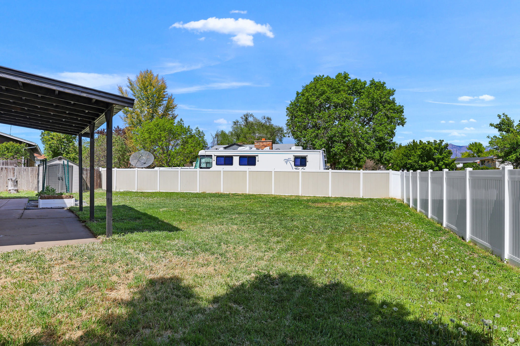 Expansive grassy yard area featuring a full vinyl fence, covered patio, and concrete patio flooring