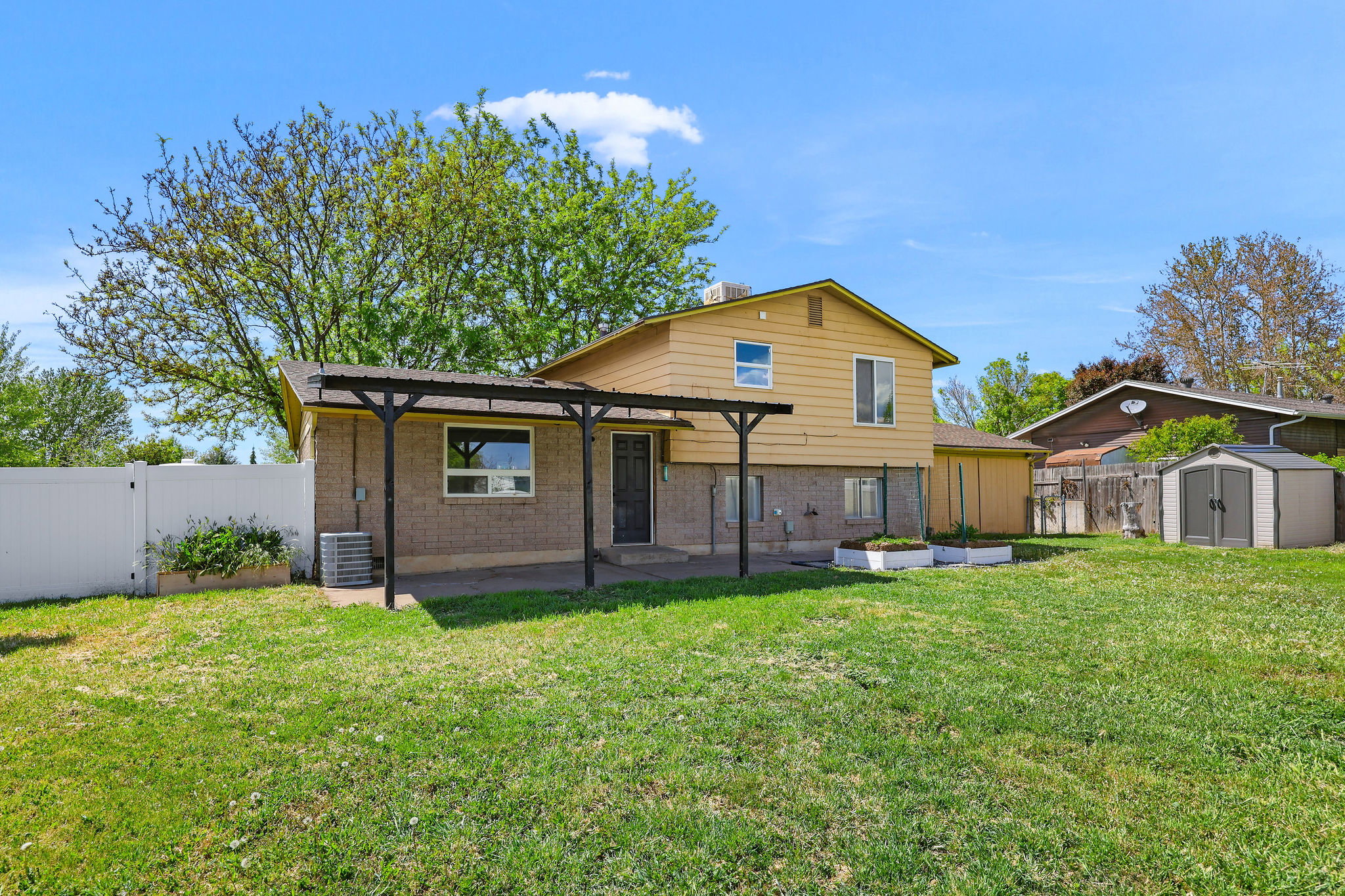 Expansive backyard with a covered patio, vinyl fencing, two raised garden beds, and a storage shed