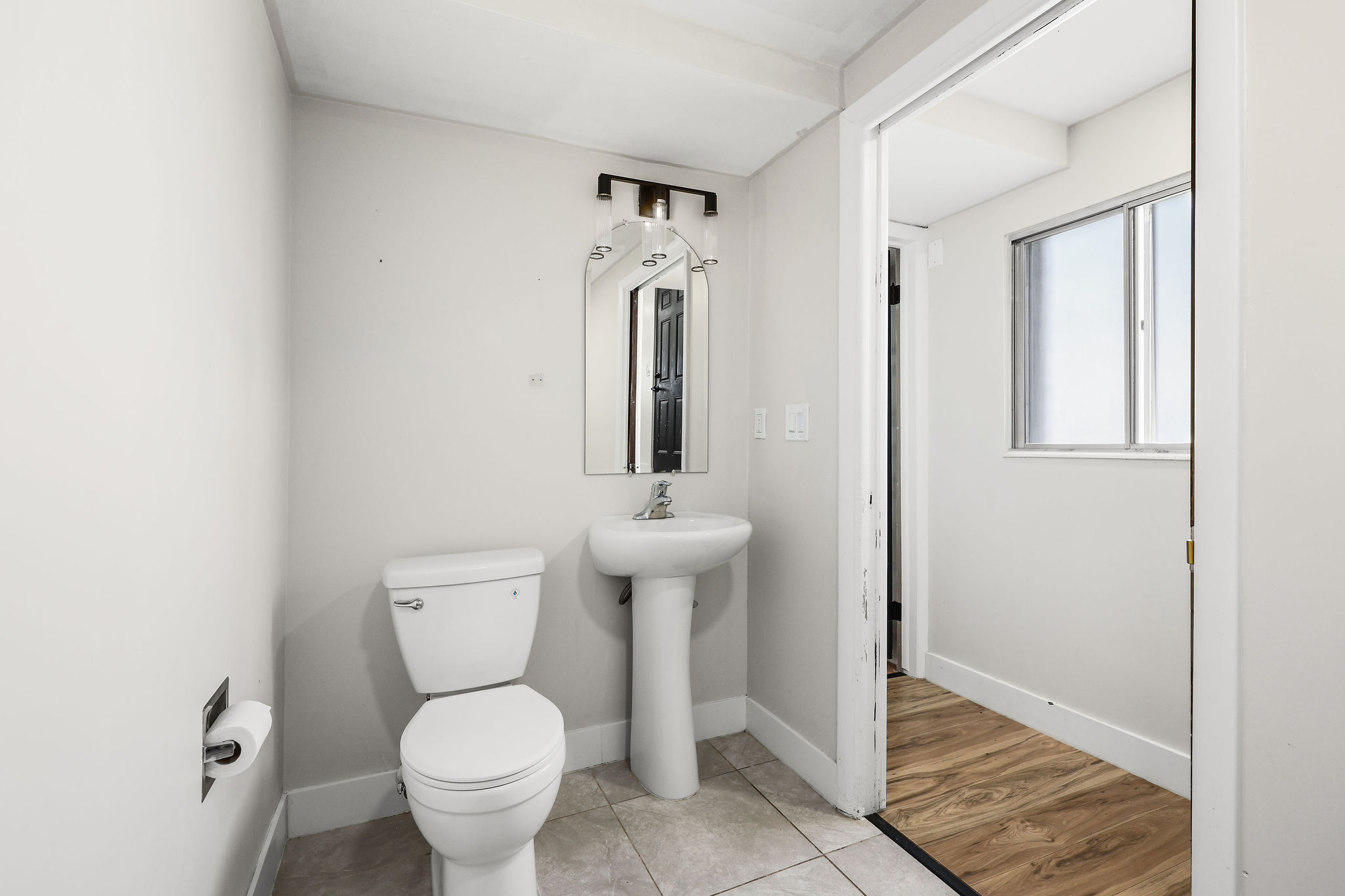Bathroom featuring a pedestal sink, toilet, wall-mounted mirror, and overhead light fixture