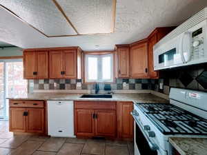Kitchen featuring wood cabinetry, a bay window, a built-in microwave, a gas range, and a tiled backsplash