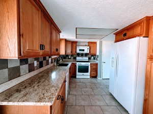 Kitchen featuring wood cabinetry, light-toned granite-style countertops, and a checkered tile backsplash