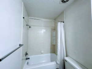 Bathroom featuring a white bathtub, ceramic wall tiling, shower head with dark-finish fixtures, and an integrated shower caddy