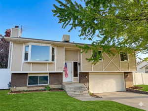 Split-level residence featuring a two-car garage with a paneled door, a bay window, and a brick foundation