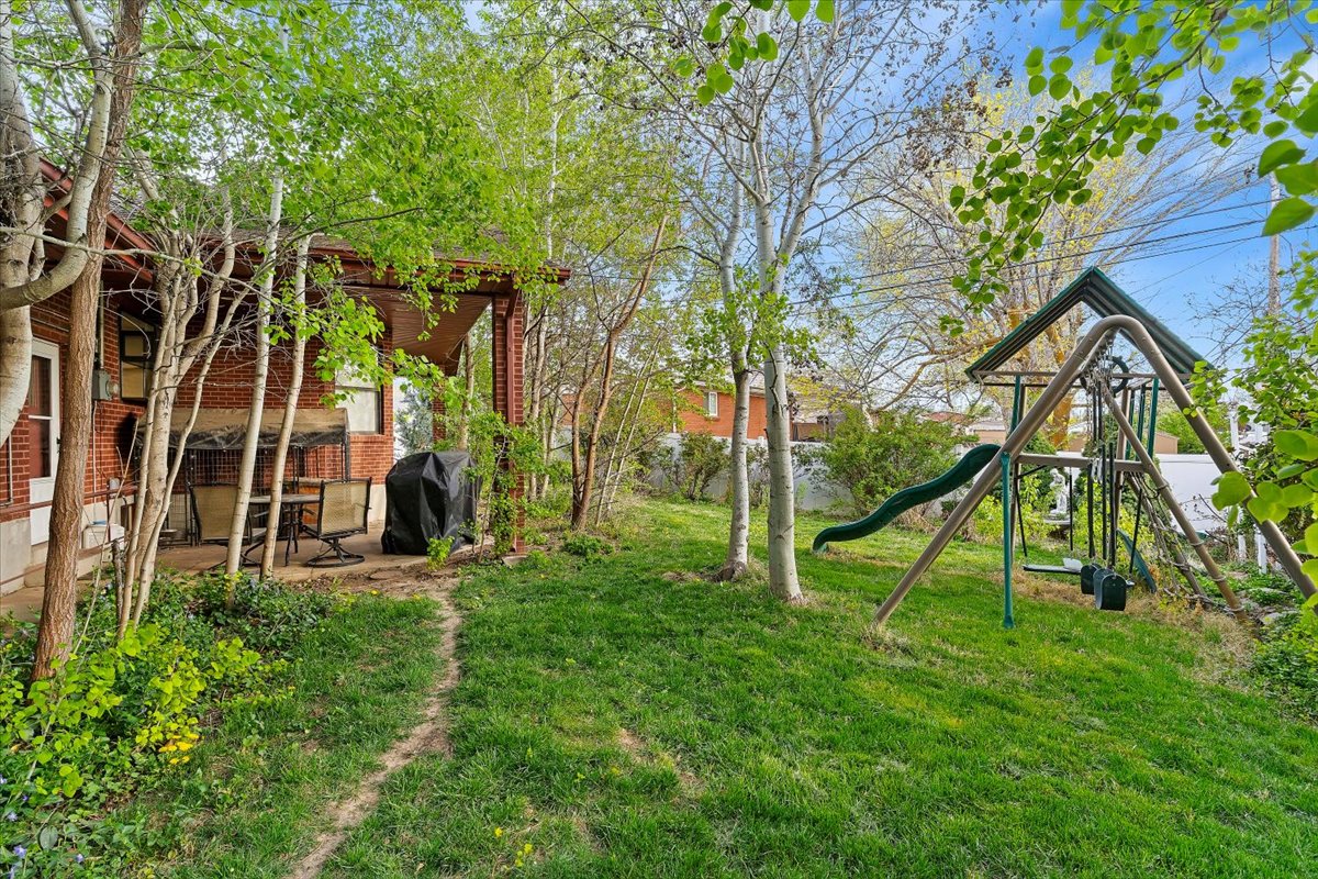 Expansive backyard featuring a lush lawn, mature trees, and a dedicated play structure with a slide