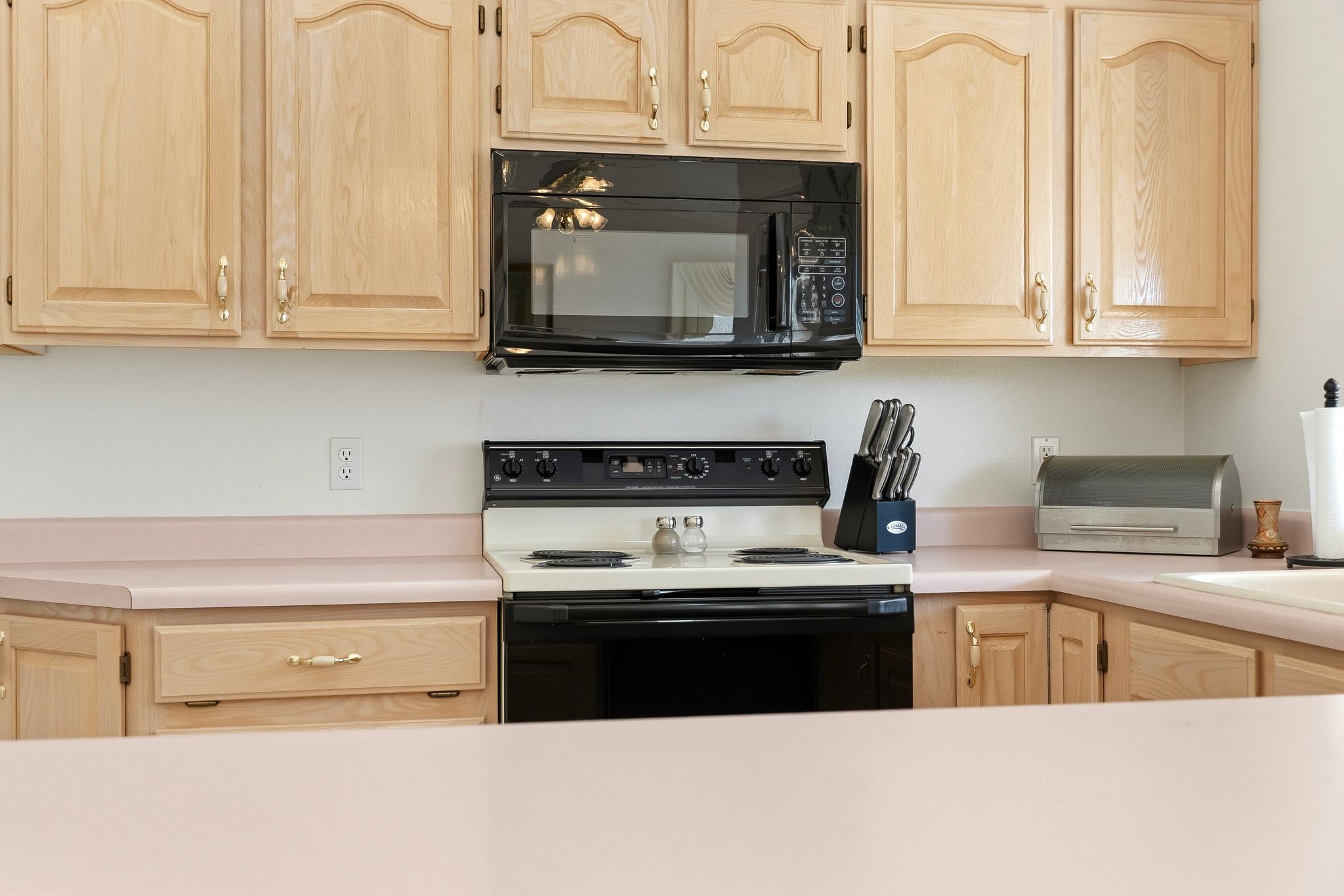 Kitchen featuring light wood cabinetry with arched top panels, a built-in microwave, and solid surface countertops