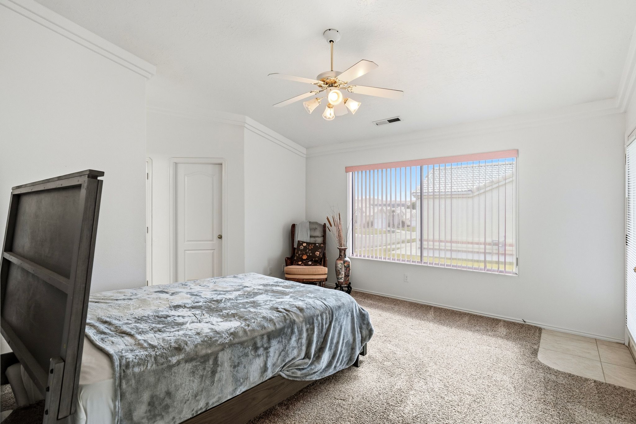 Bright interior space featuring a large window with vertical blinds, crown molding, a ceiling fan with integrated lighting, and carpeted flooring