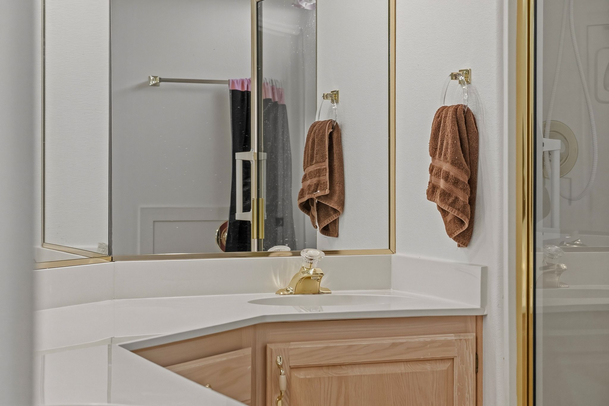 Bathroom vanity featuring a corner sink, light wood cabinetry, white countertop, and gold-finish fixtures