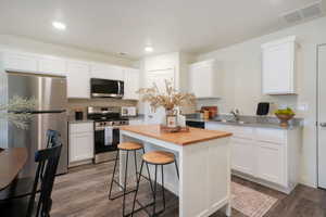 Contemporary kitchen featuring white cabinetry, stainless steel appliances, granite-style countertops, wood-finish flooring, and a central island with a butcher block top