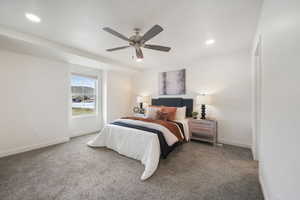 Spacious bedroom featuring neutral wall tones, gray carpet, a ceiling fan with integrated lighting, recessed overhead lighting, and a large window offering distant mountain and water scenery