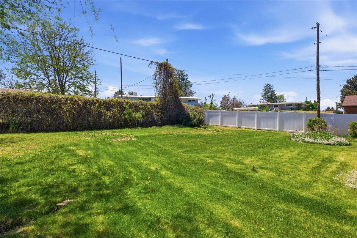 Spacious grassy yard featuring a white privacy fence along one side and natural foliage along the other