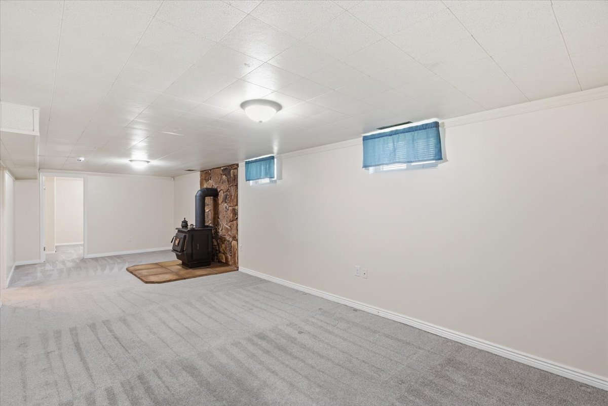 Spacious room featuring a central wood-burning stove with a stone surround, light gray patterned carpeting, and white painted walls