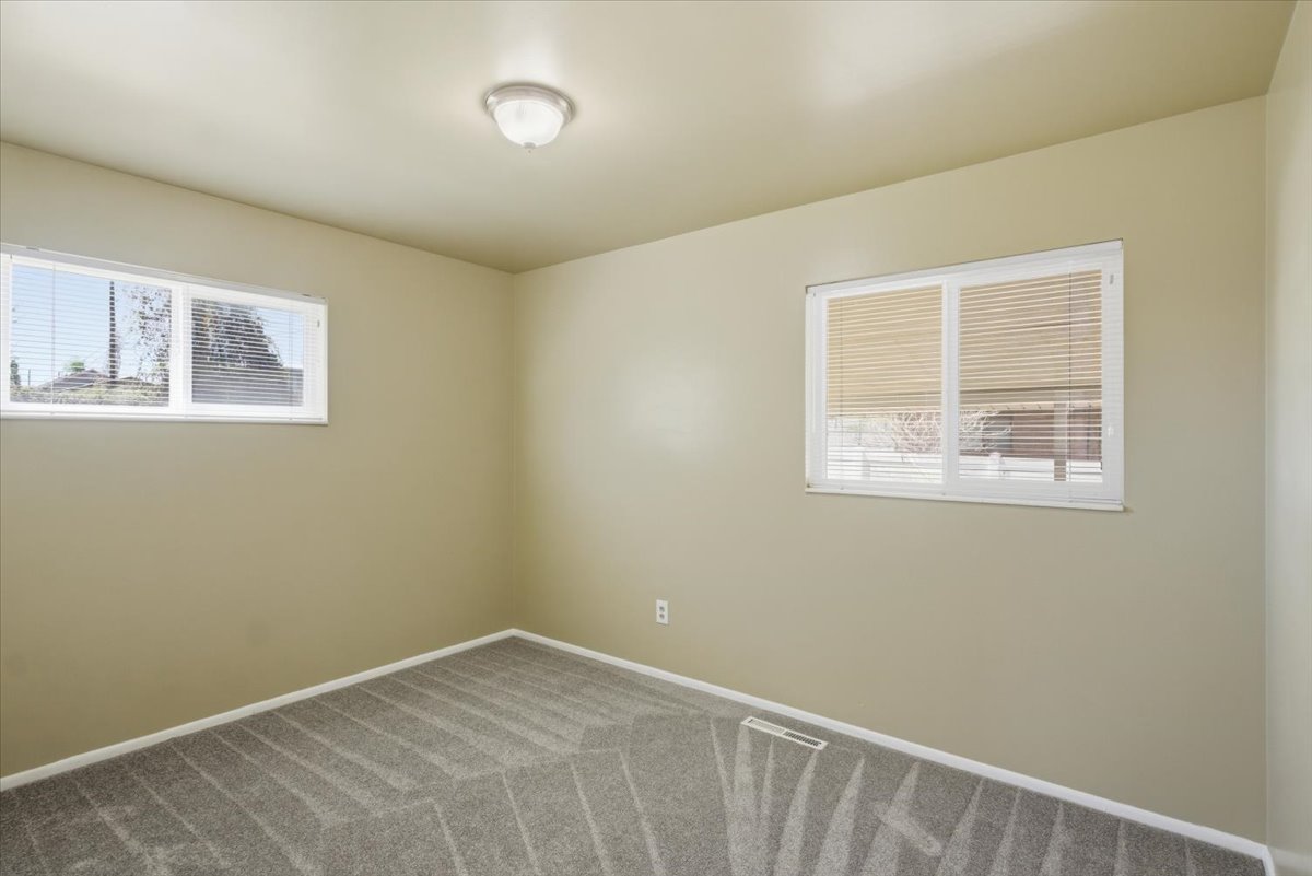 Neutral-toned room featuring a semi-flush mount ceiling light, two windows with white frames, and grey patterned carpet