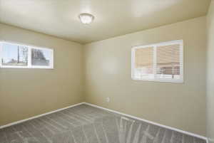 Neutral-toned room featuring a semi-flush mount ceiling light, two windows with white frames, and grey patterned carpet