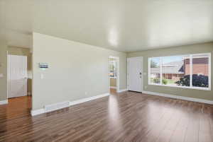 Spacious living area featuring wood-finish flooring, a large picture window, and a white paneled entry door