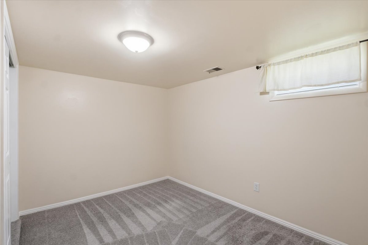 Carpeted interior space with a flush-mount ceiling light fixture, a window with a valance, a white door frame, and white baseboards